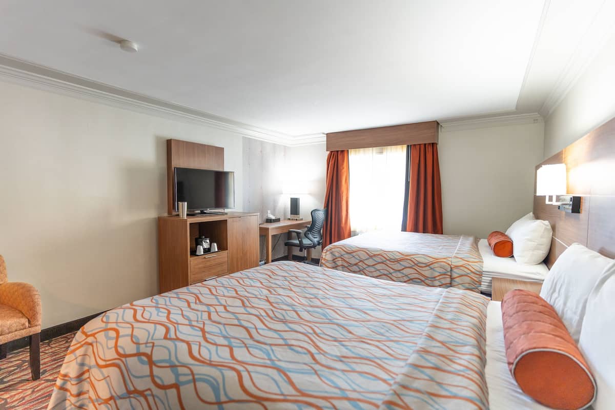 A hotel room with two beds, a desk, a television, and a chair.