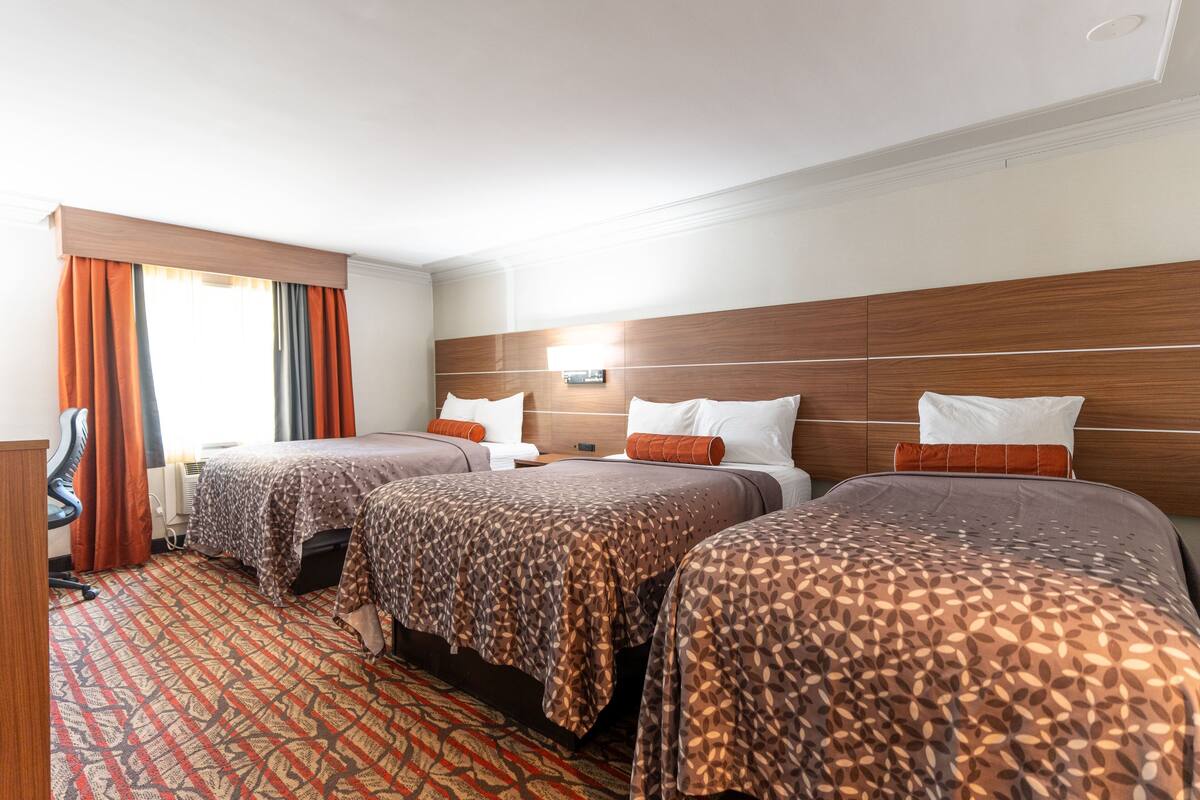 A hotel room with three beds, a desk, and a patterned carpet.