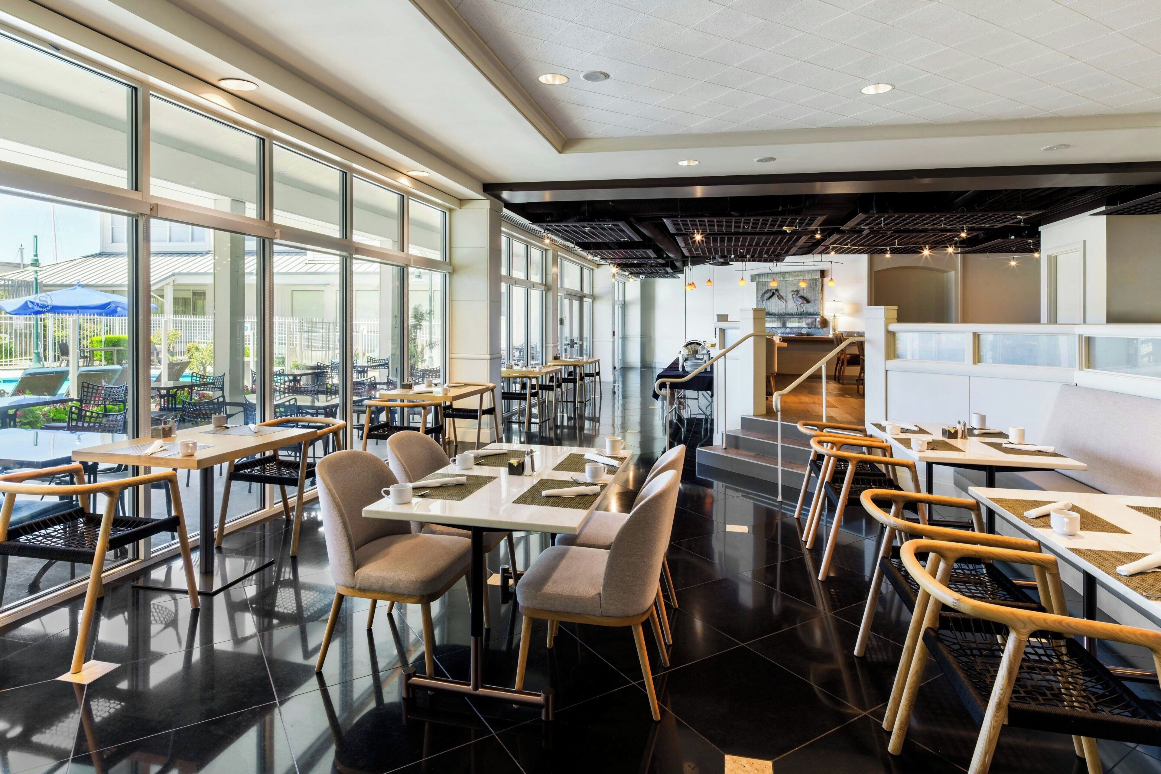 A modern restaurant interior with large windows, black tiled floors, and a mix of wooden and metal furniture.