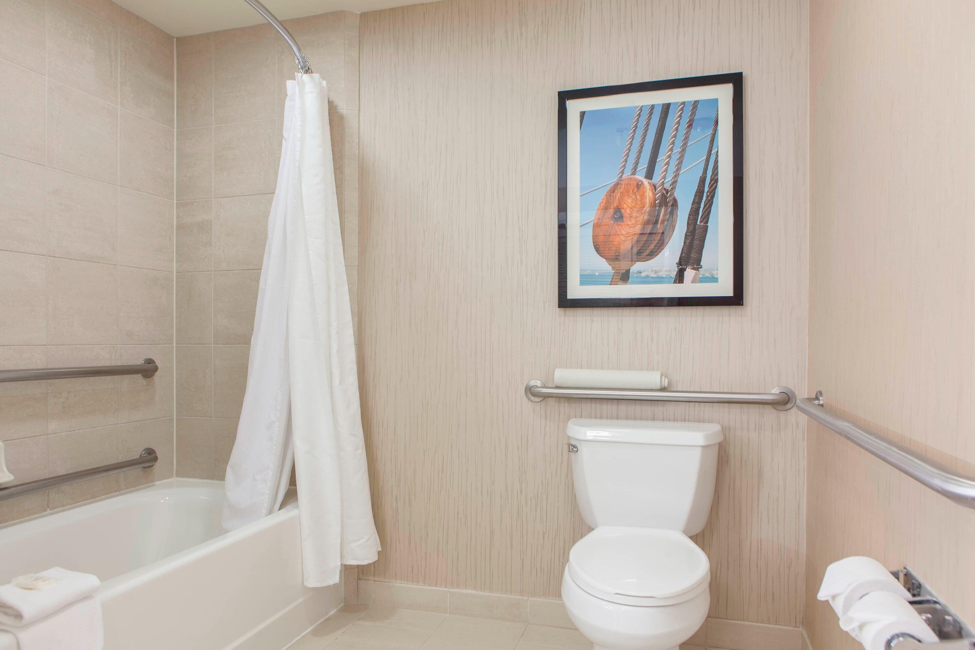 A bathroom with a bathtub, toilet, and a framed picture on the wall.