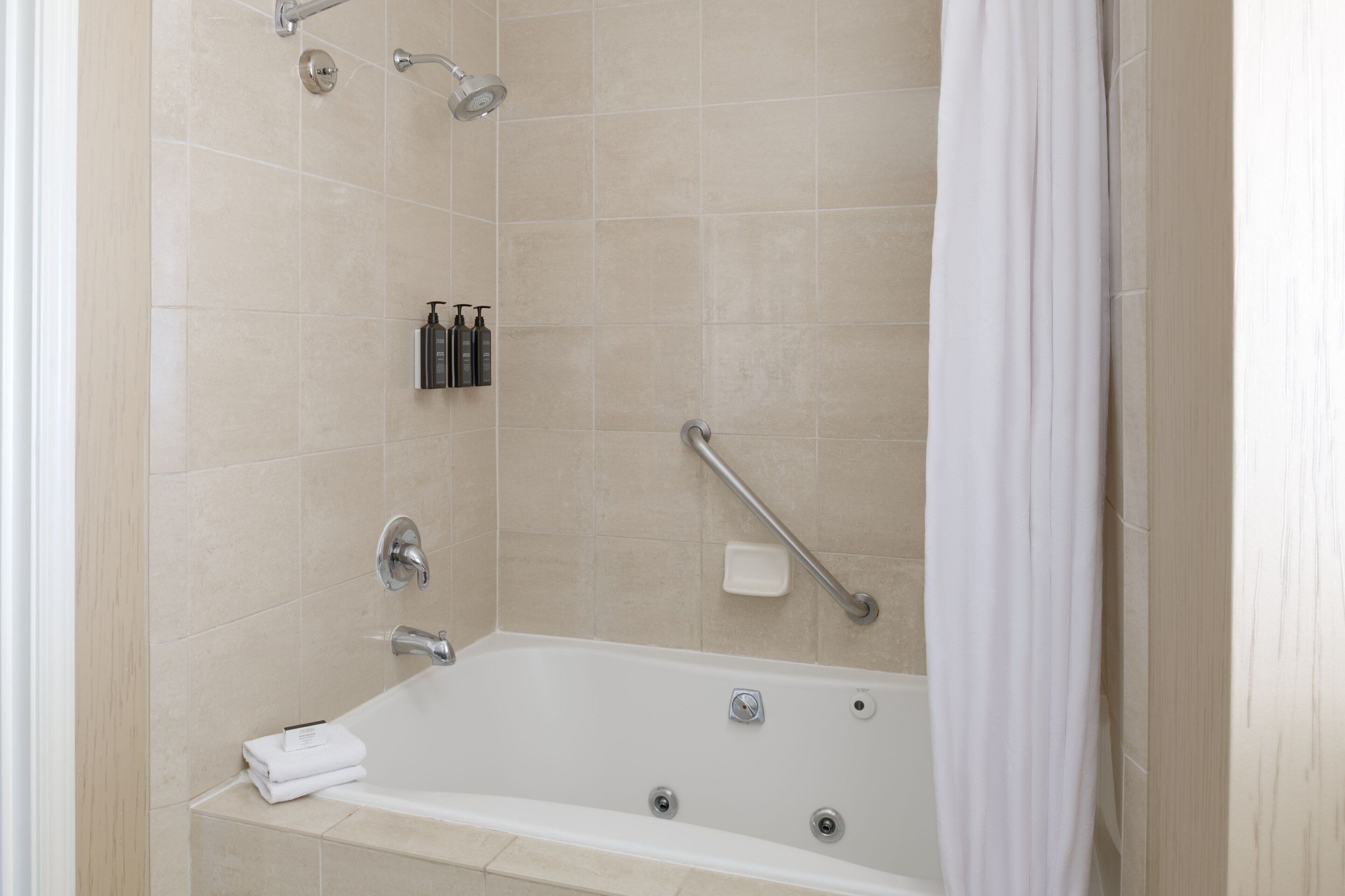 A modern bathroom with a bathtub, a showerhead, a handrail, and a soap dish.