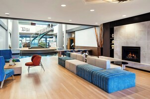 A modern hotel lobby with a fireplace, seating area, and a staircase leading to an upper level.