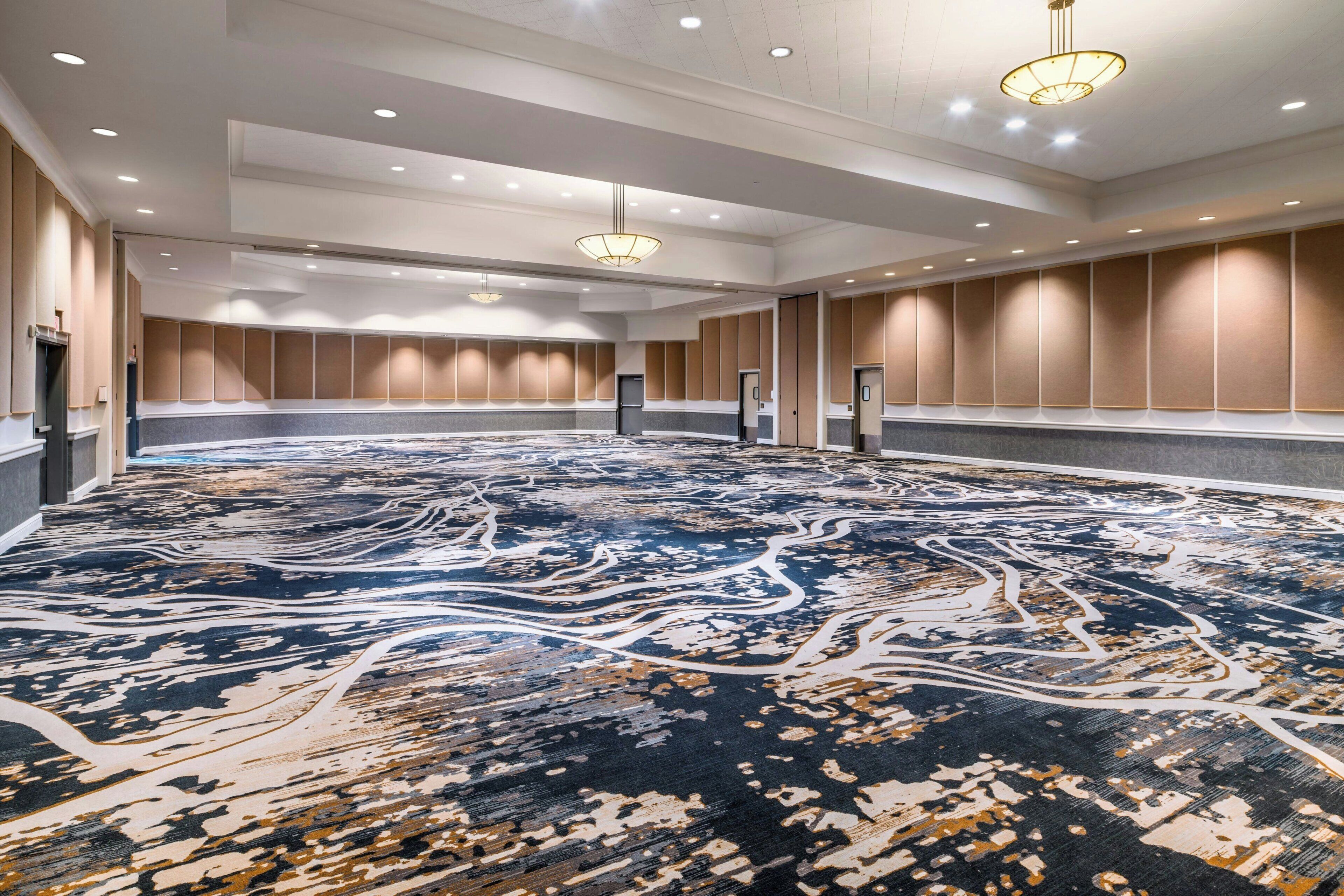 A spacious conference room with a patterned carpet, recessed lighting, and a modern chandelier.