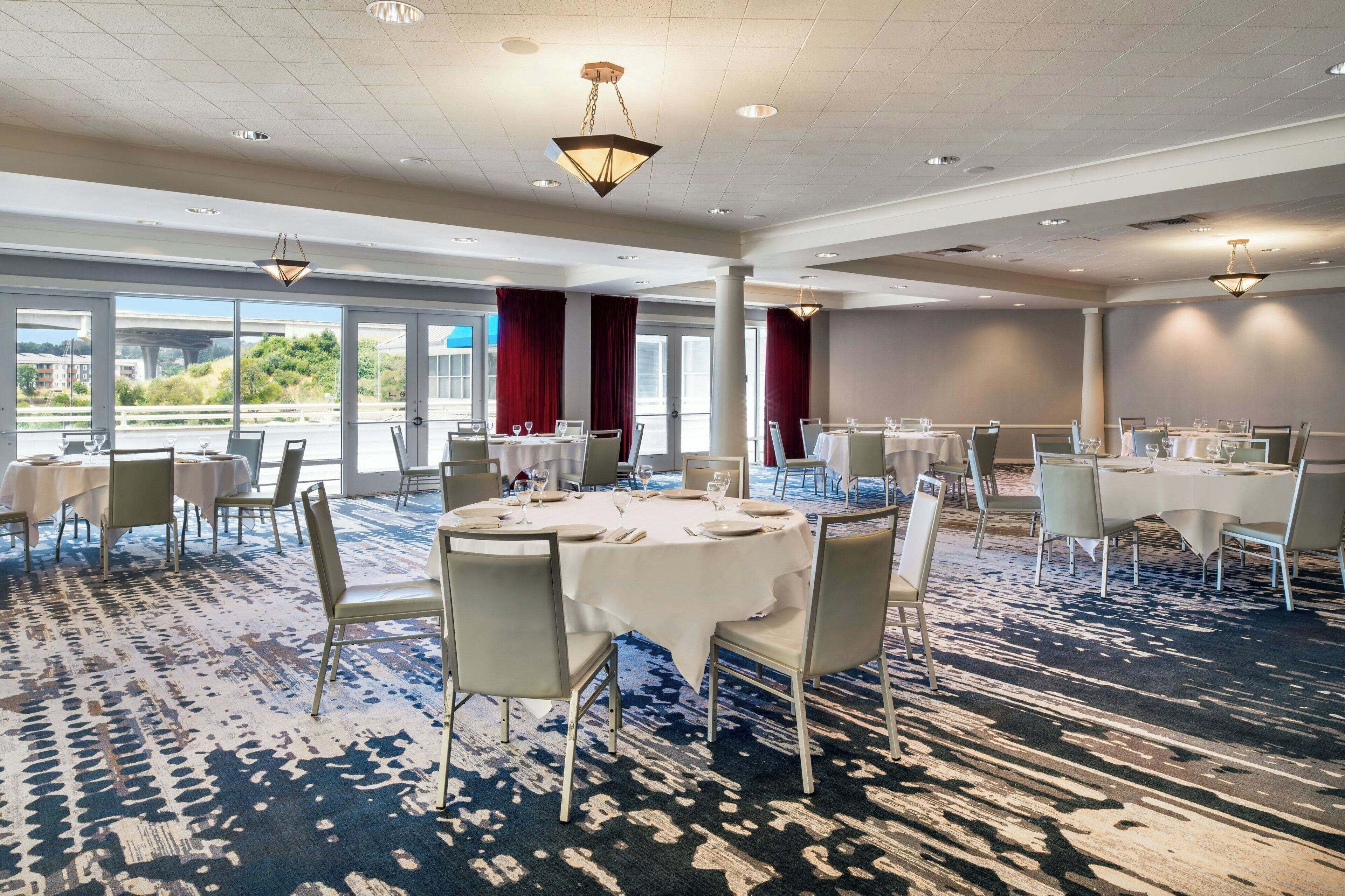 Une salle à manger d’hôtel avec des tables rondes, des chaises et un tapis à motifs.