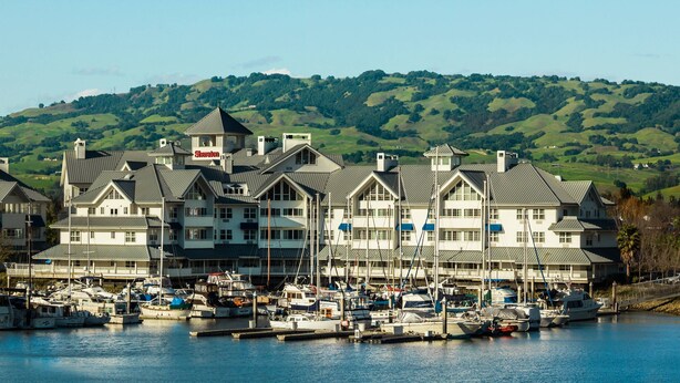 Un puerto deportivo con varias embarcaciones amarradas, un gran hotel con un letrero que dice "Shandon", y un telón de fondo de colinas verdes.