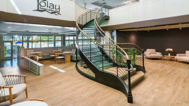 A modern interior with a curved staircase, seating areas, and a sign reading 'Sonoma County Cuisine'.