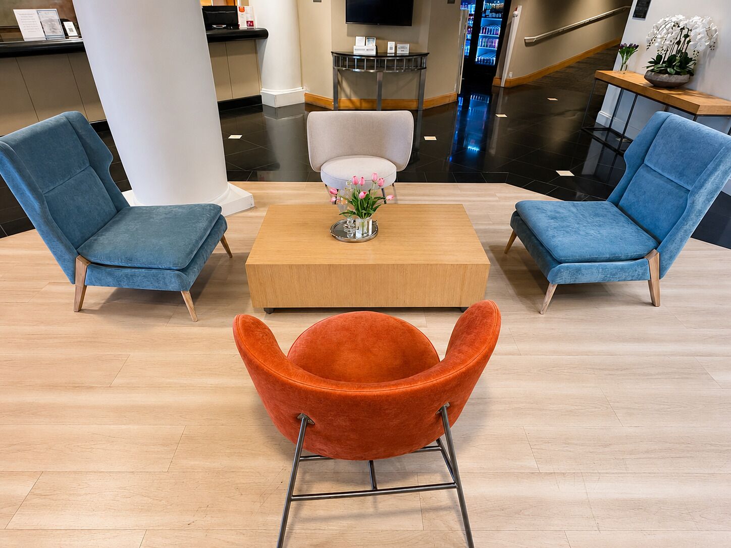 Un hall con dos sillones azules, una mesa de centro de madera y una butaca naranja.