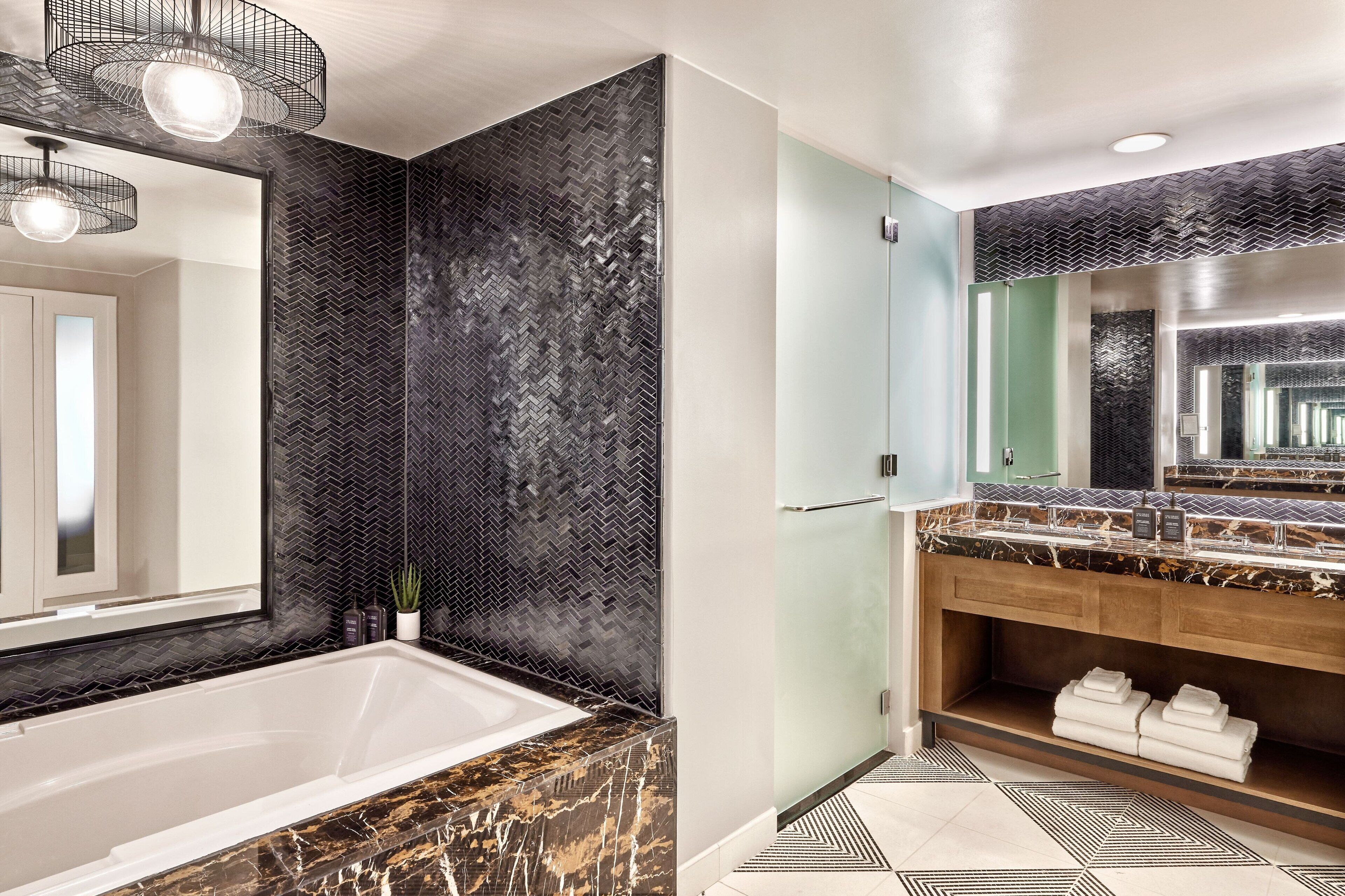 A modern bathroom with a large bathtub, a herringbone-patterned wall, a vanity with a mirror, and a geometric-patterned floor.