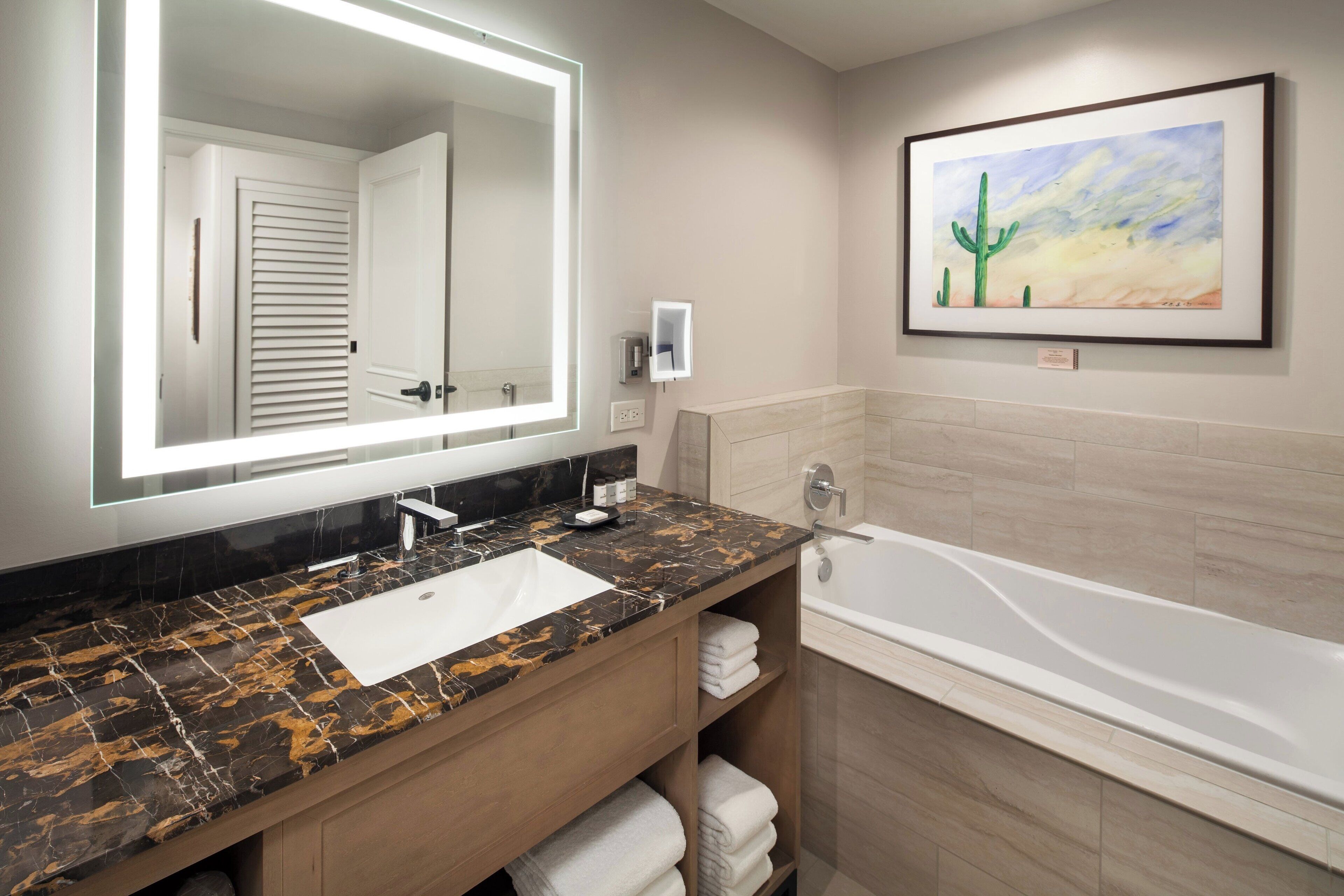 Une salle de bain avec un lavabo en marbre, un grand miroir, un tableau encadré et une baignoire.