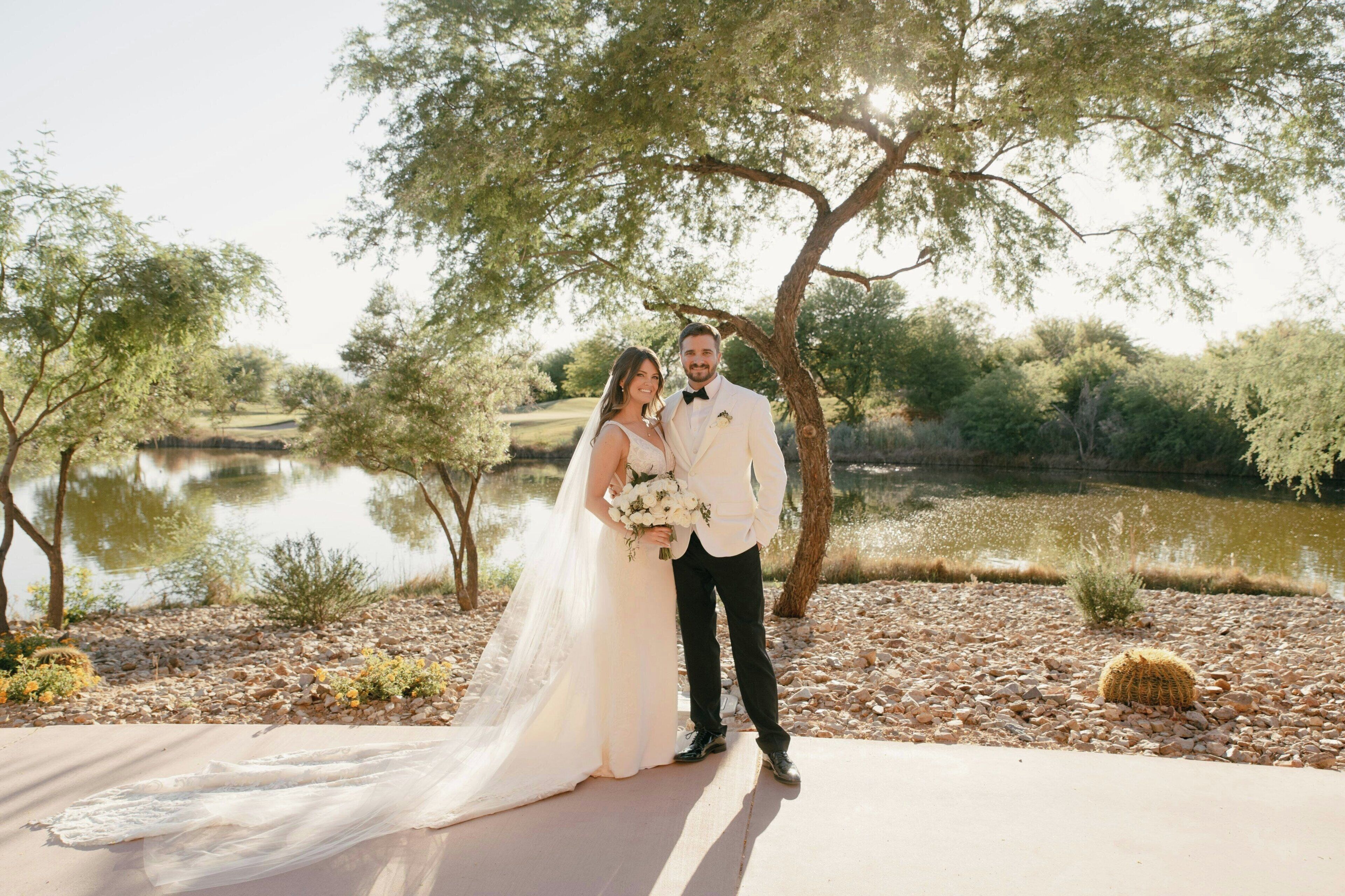 A couple standing on a concrete path with a body of water and trees in the background.