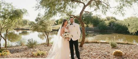 A couple standing on a concrete path with a body of water and trees in the background.