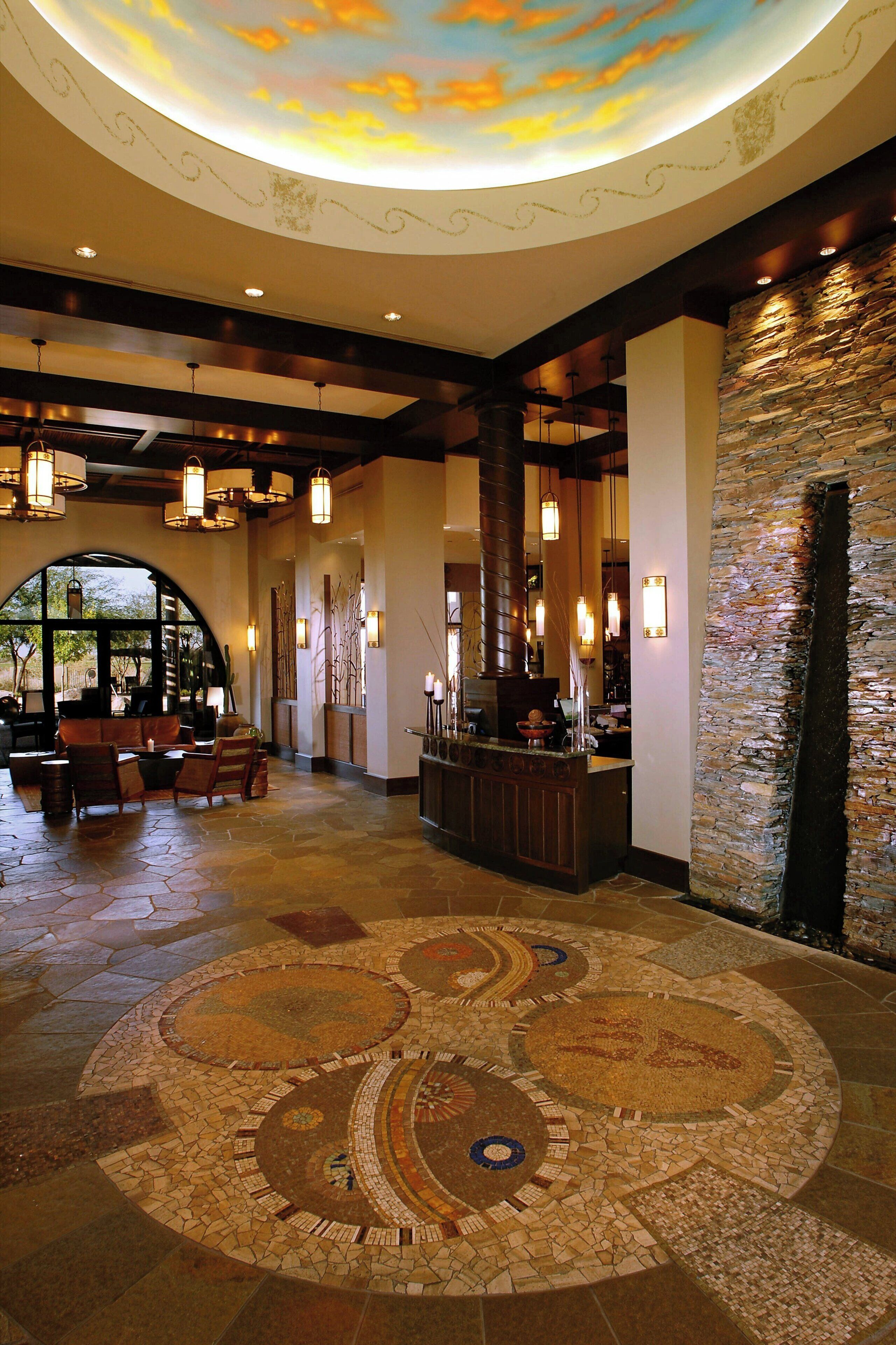 A lobby with a mosaic floor, a reception desk, and a stone wall.