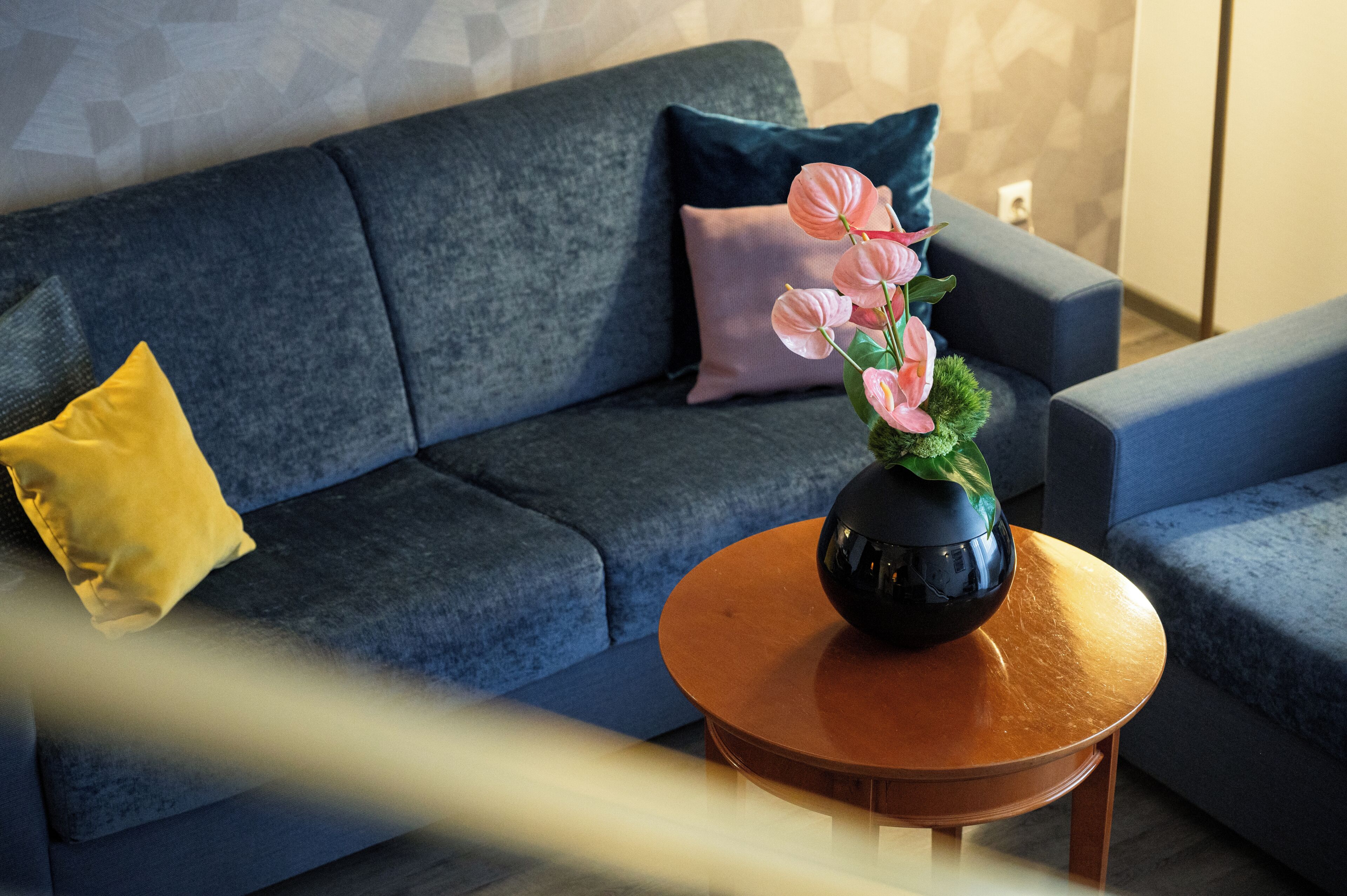 Ein modernes Wohnzimmer mit einem dunkelblauen Sofa, einem runden Holztisch und einer Vase mit rosa Blumen.