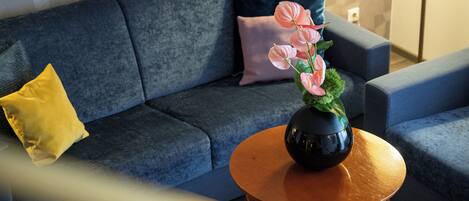 Ein modernes Wohnzimmer mit einem dunkelblauen Sofa, einem runden Holztisch und einer Vase mit rosa Blumen.
