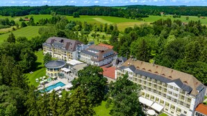 A large hotel with multiple buildings, a swimming pool, and surrounding green fields and trees. - Der Sonnenhof (Bad Woerishofen)