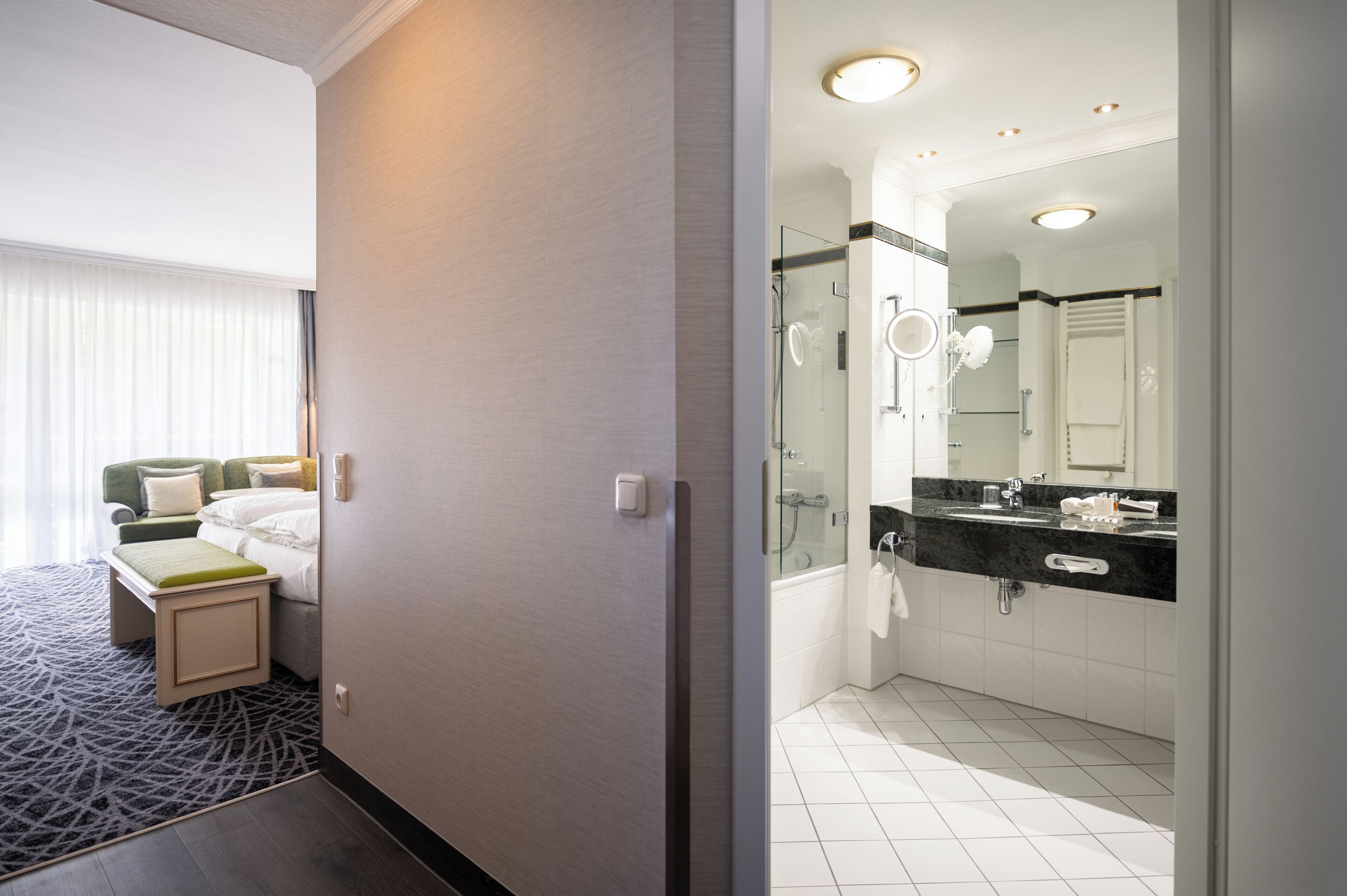A hotel room with a bed, bedside table, and a bathroom with a shower, sink, and mirror.