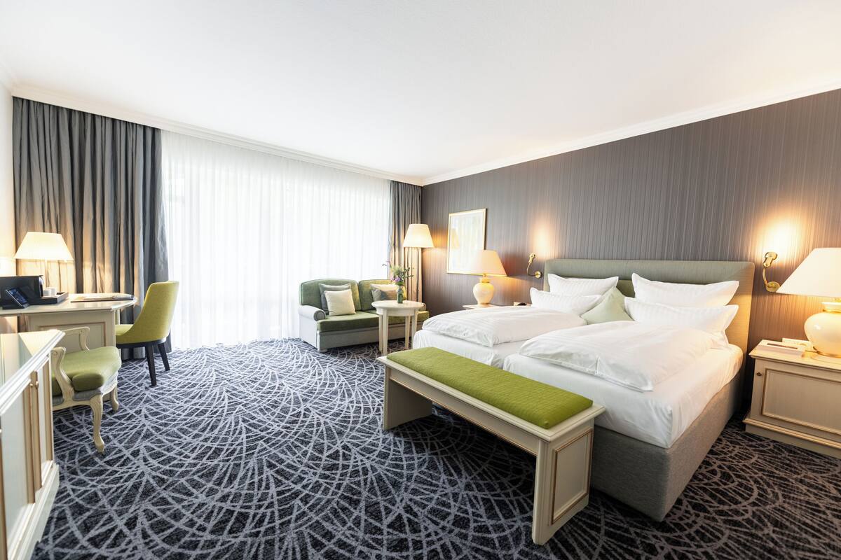 A hotel room with a large bed, a desk, a chair, a bench, and two bedside tables with lamps.