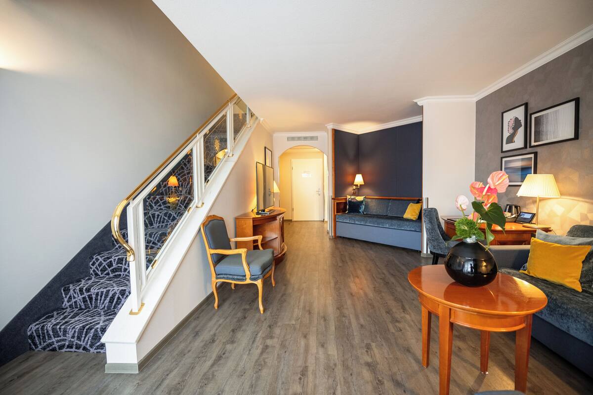 A modern living room with a staircase, a sofa set, a coffee table, and a vase with flowers.