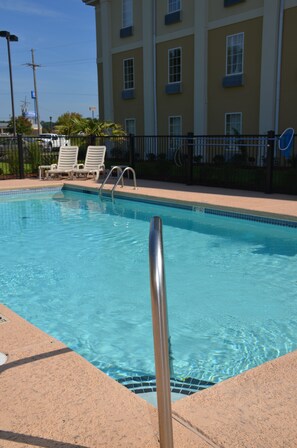 A swimming pool with clear blue water, surrounded by a tiled deck and a metal railing.