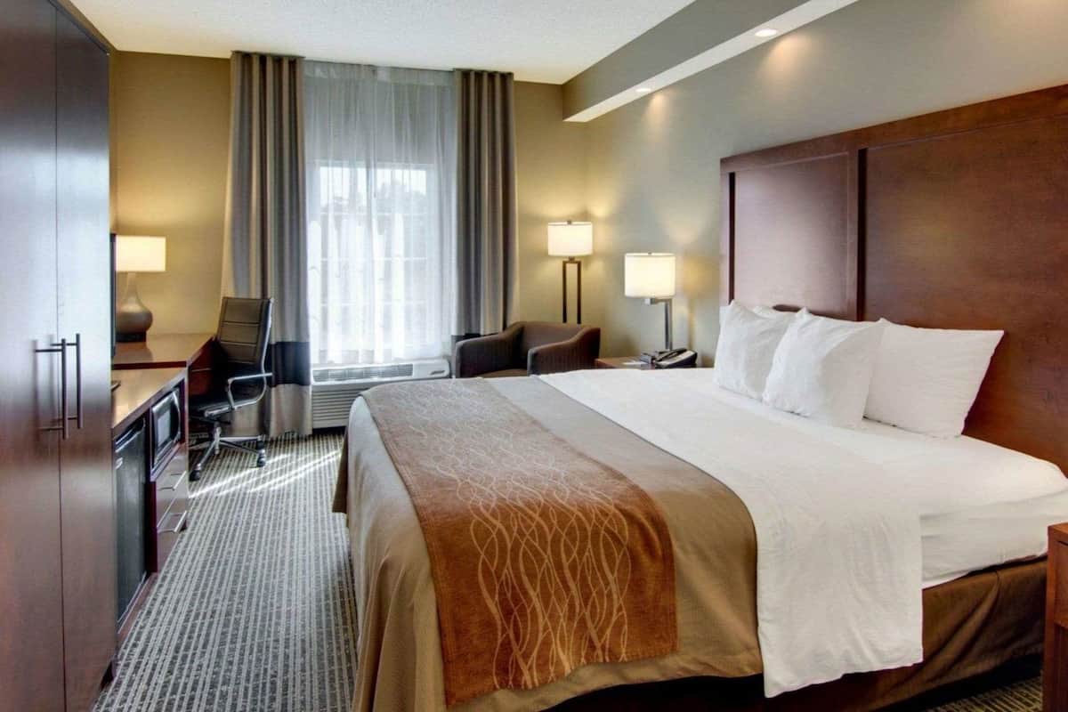 A hotel room with a large bed, a desk, a chair, two bedside lamps, and a window with curtains.
