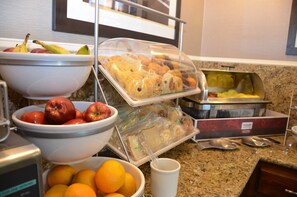 A breakfast buffet with various fruits, pastries, and sandwiches.