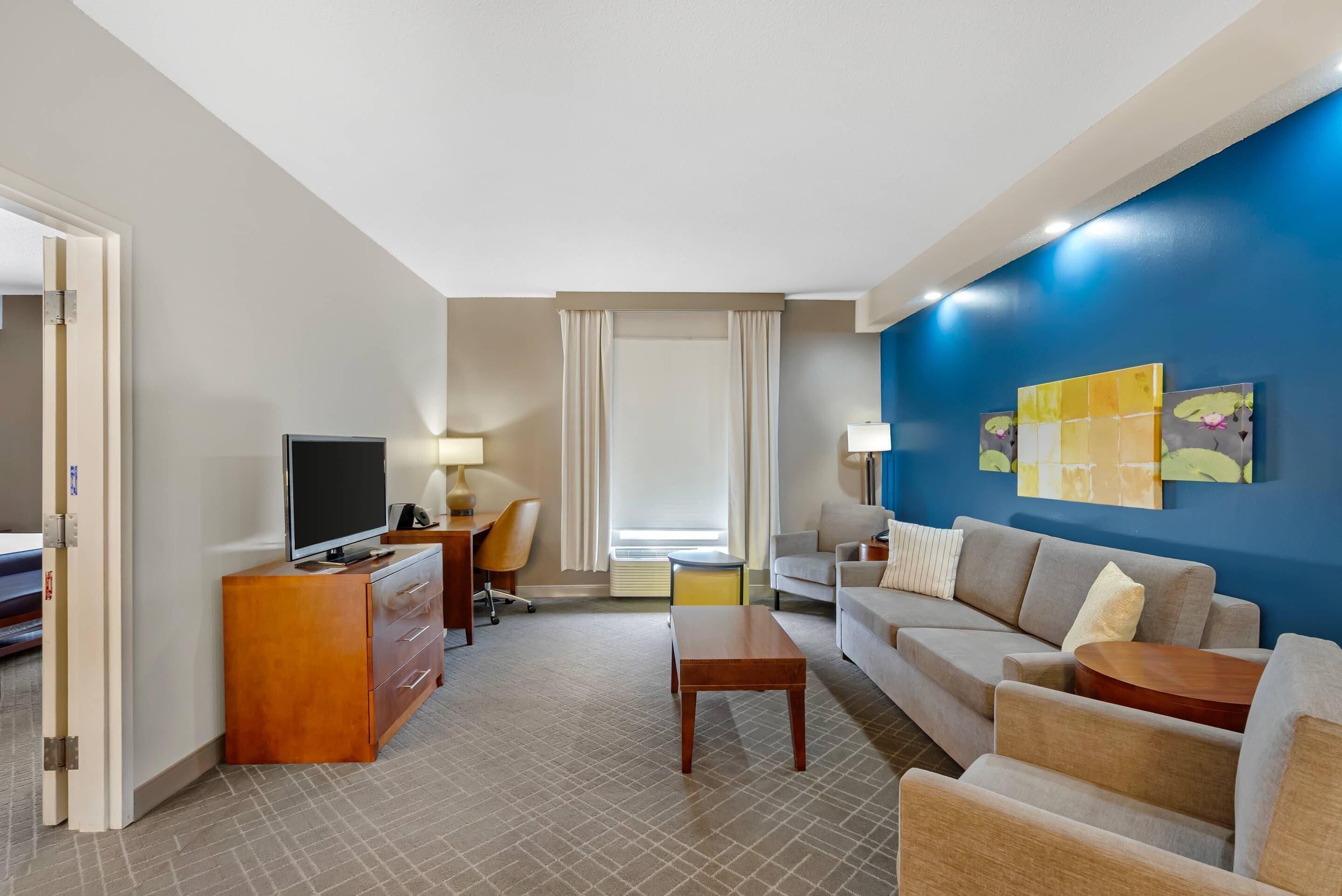 Habitación de hotel con televisión, escritorio, sofá y mesa de centro.