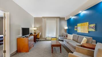 Habitación de hotel con televisión, escritorio, sofá y mesa de centro.