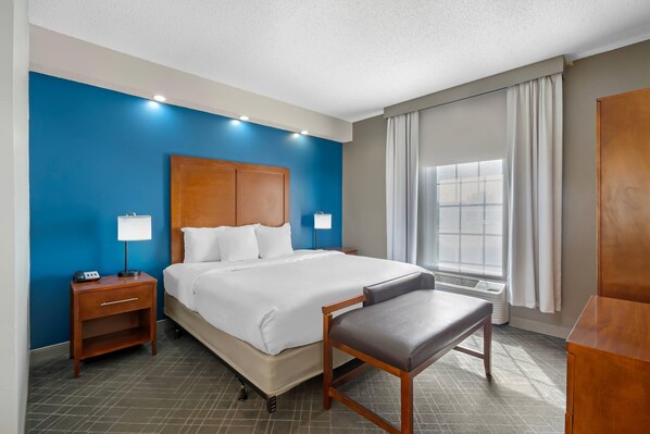 A hotel room with a large bed, bedside tables, a desk, a chair, and a window with curtains.