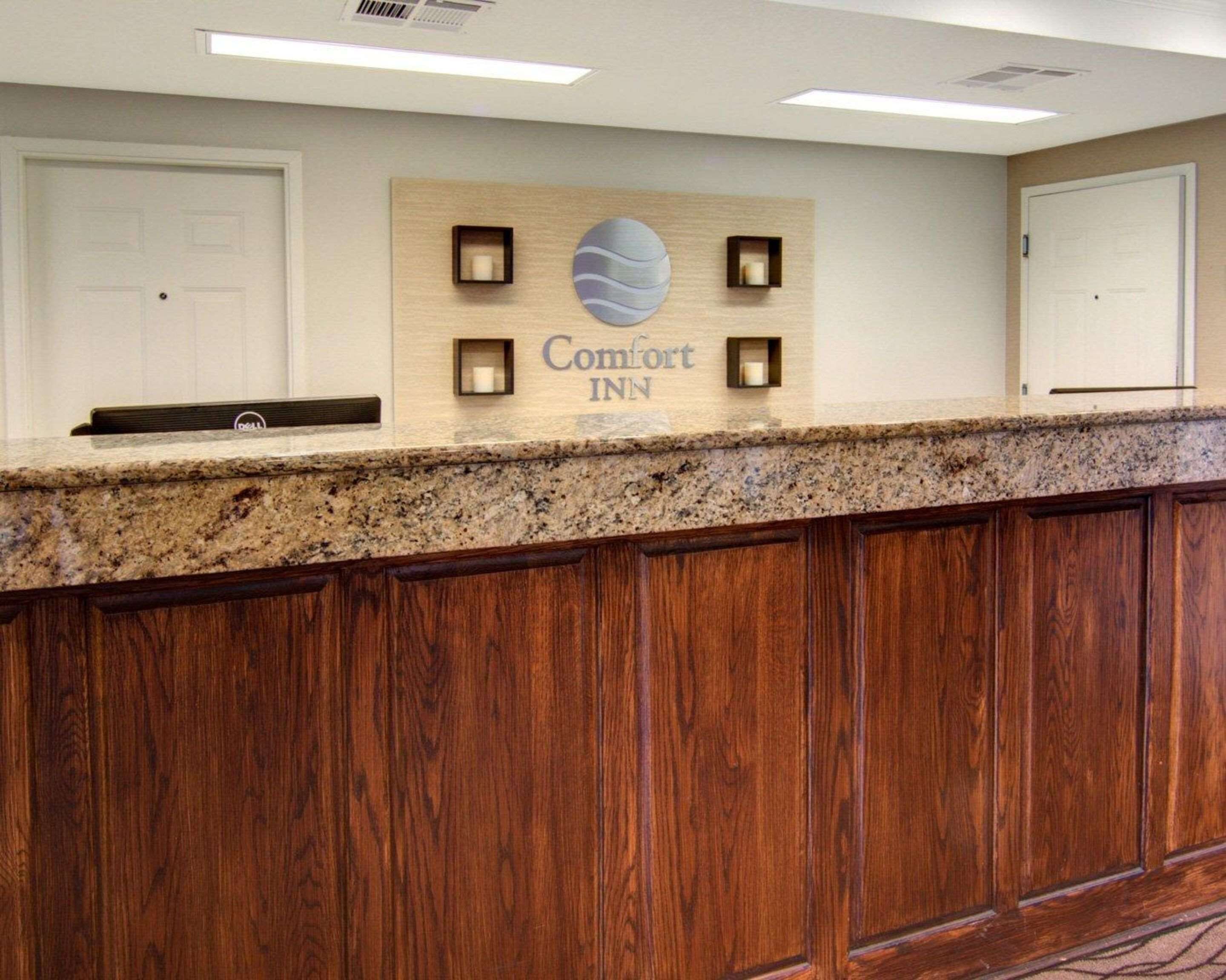 A reception desk with a sign reading "Comfort Inn" and a logo, wooden paneling, and a marble countertop.