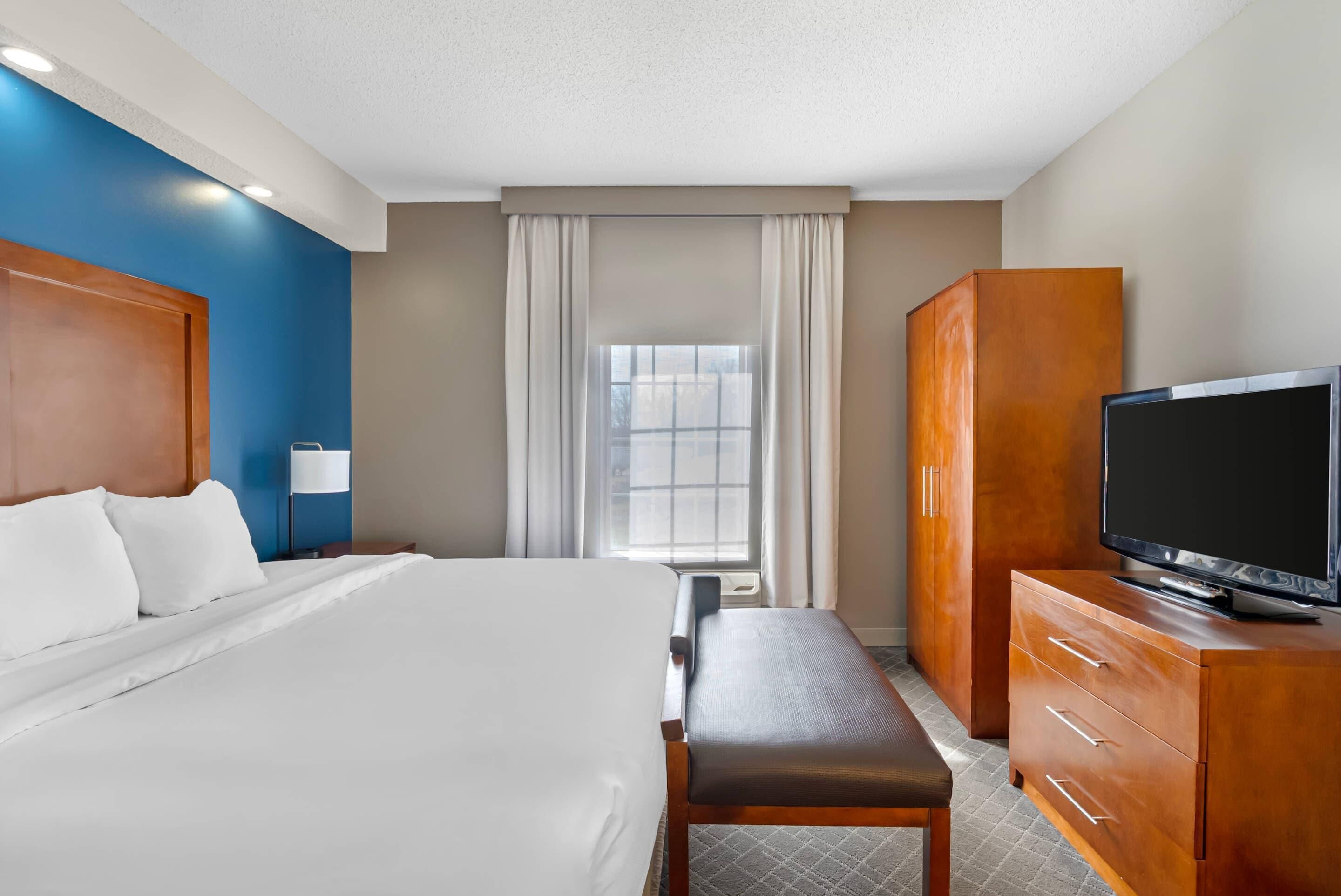 A hotel room with a large bed, a wooden wardrobe, a television, and a window with curtains.