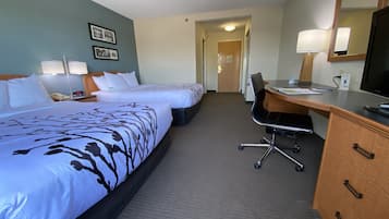 A hotel room with two beds, a desk, a chair, a dresser, a mirror, and two lamps.