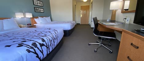 A hotel room with two beds, a desk, a chair, a dresser, a mirror, and two lamps.