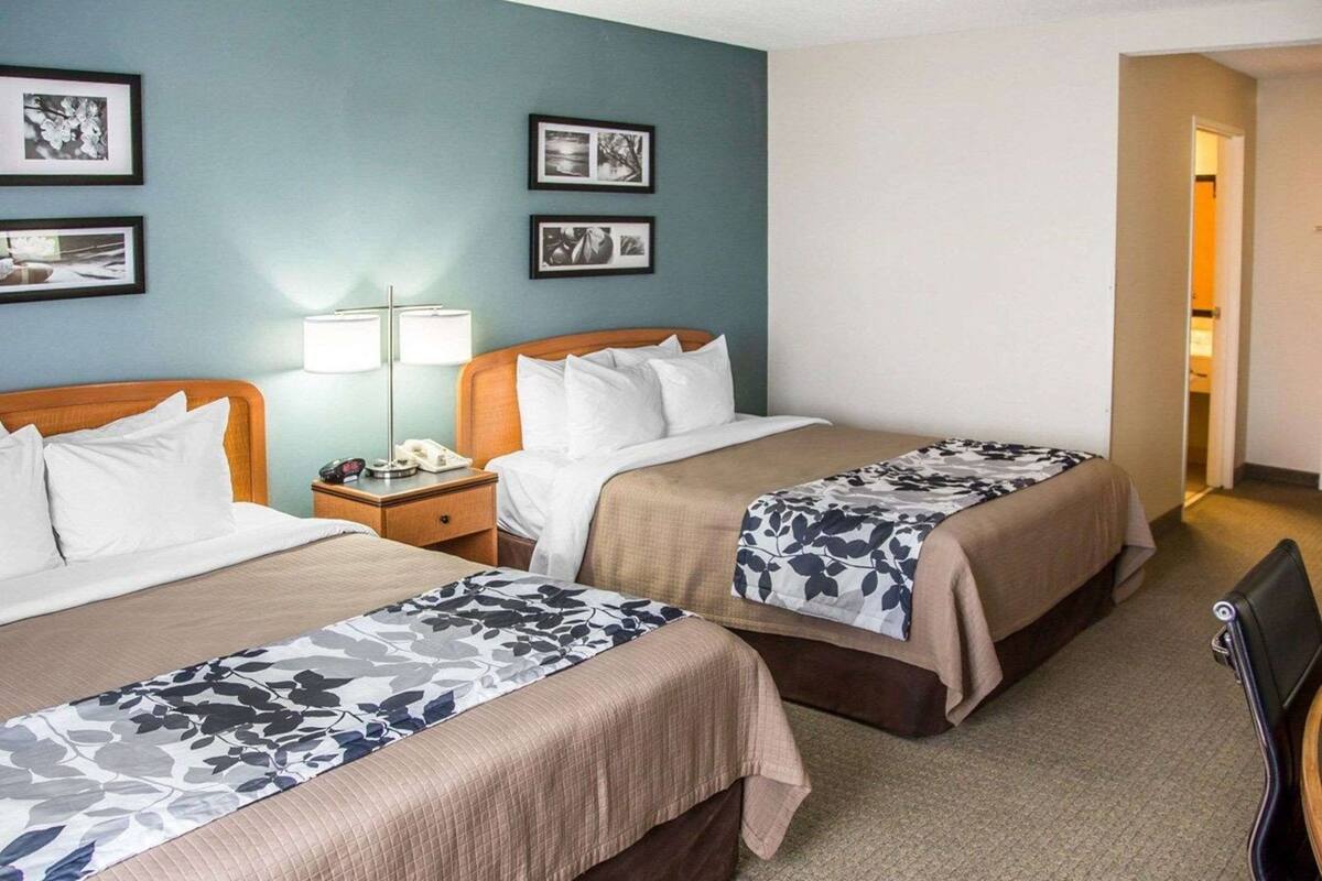 Una habitación de hotel con dos camas, una mesita de noche con lámpara y cuadros en la pared.
