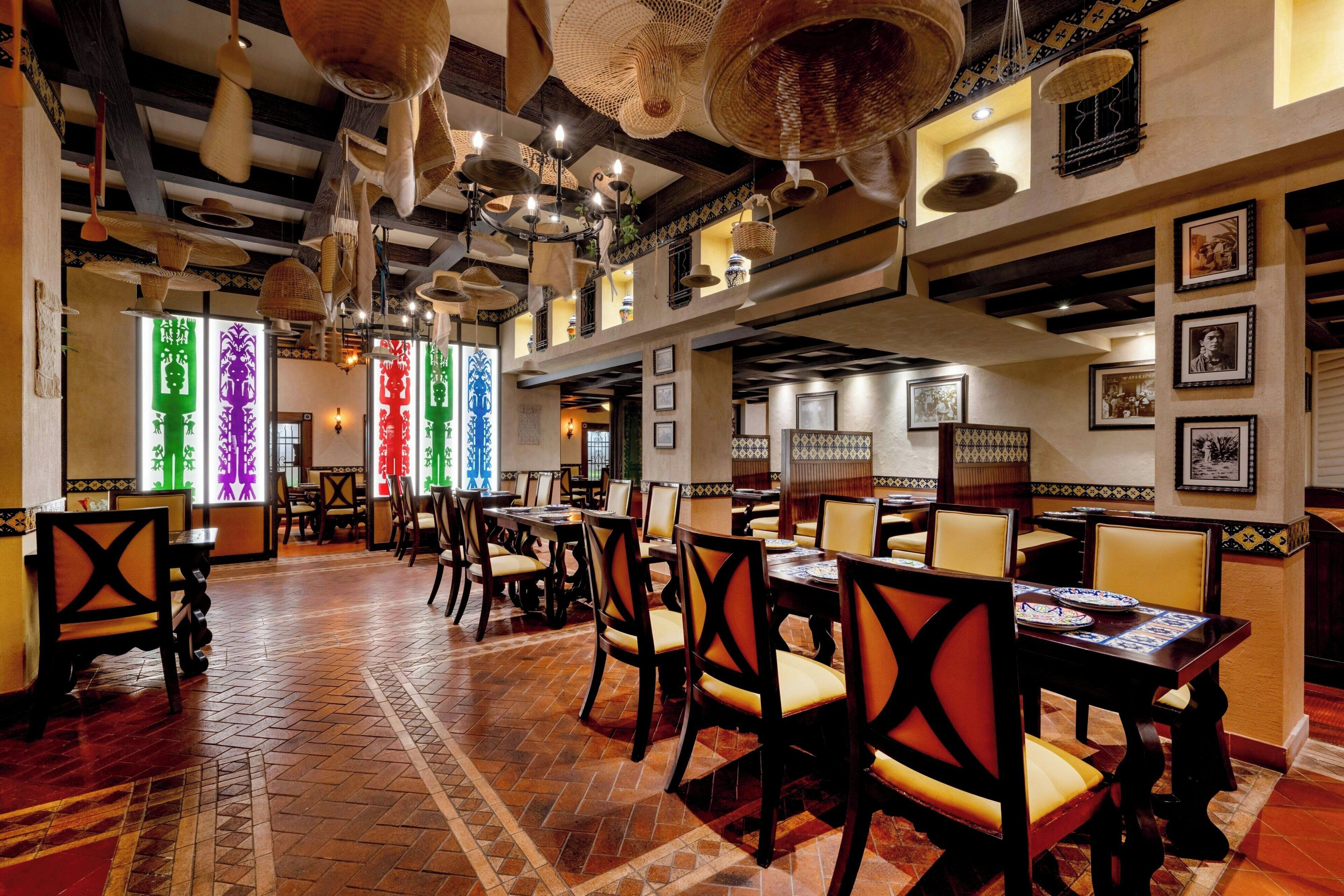 A restaurant with high ceilings, hanging baskets, and traditional decor. Tables and chairs are arranged for dining.