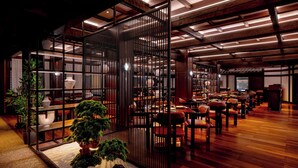 Un restaurante espacioso con suelo de madera, varias mesas y sillas. Hay plantas en macetas y una valla decorativa en el centro.