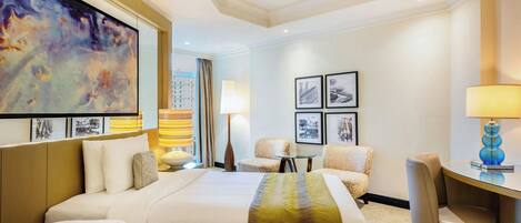 A hotel room with two beds, a desk, a chair, a lamp, and framed pictures on the wall.