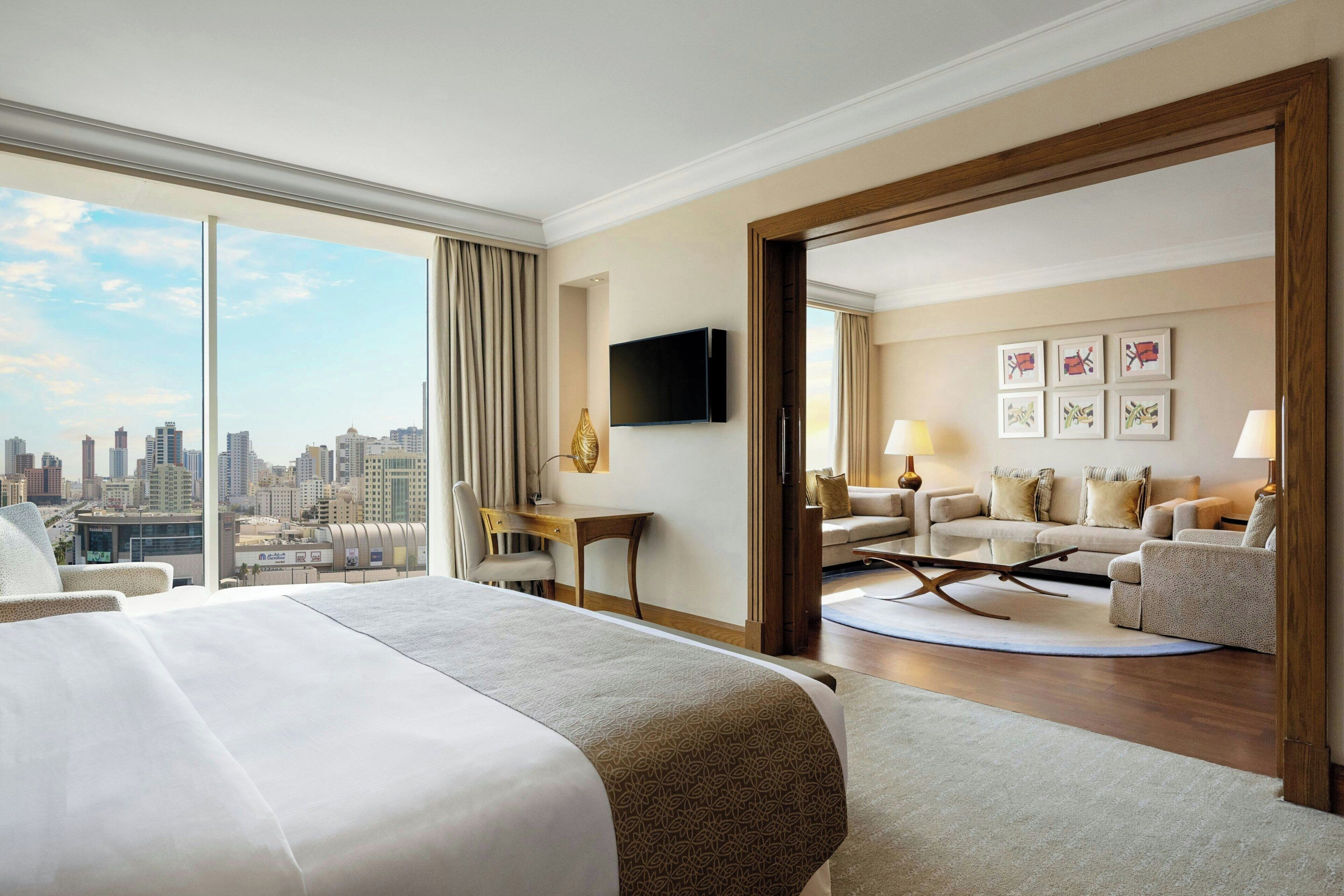 A hotel room with a large bed, a desk, a TV, a sofa, and a view of the city skyline.