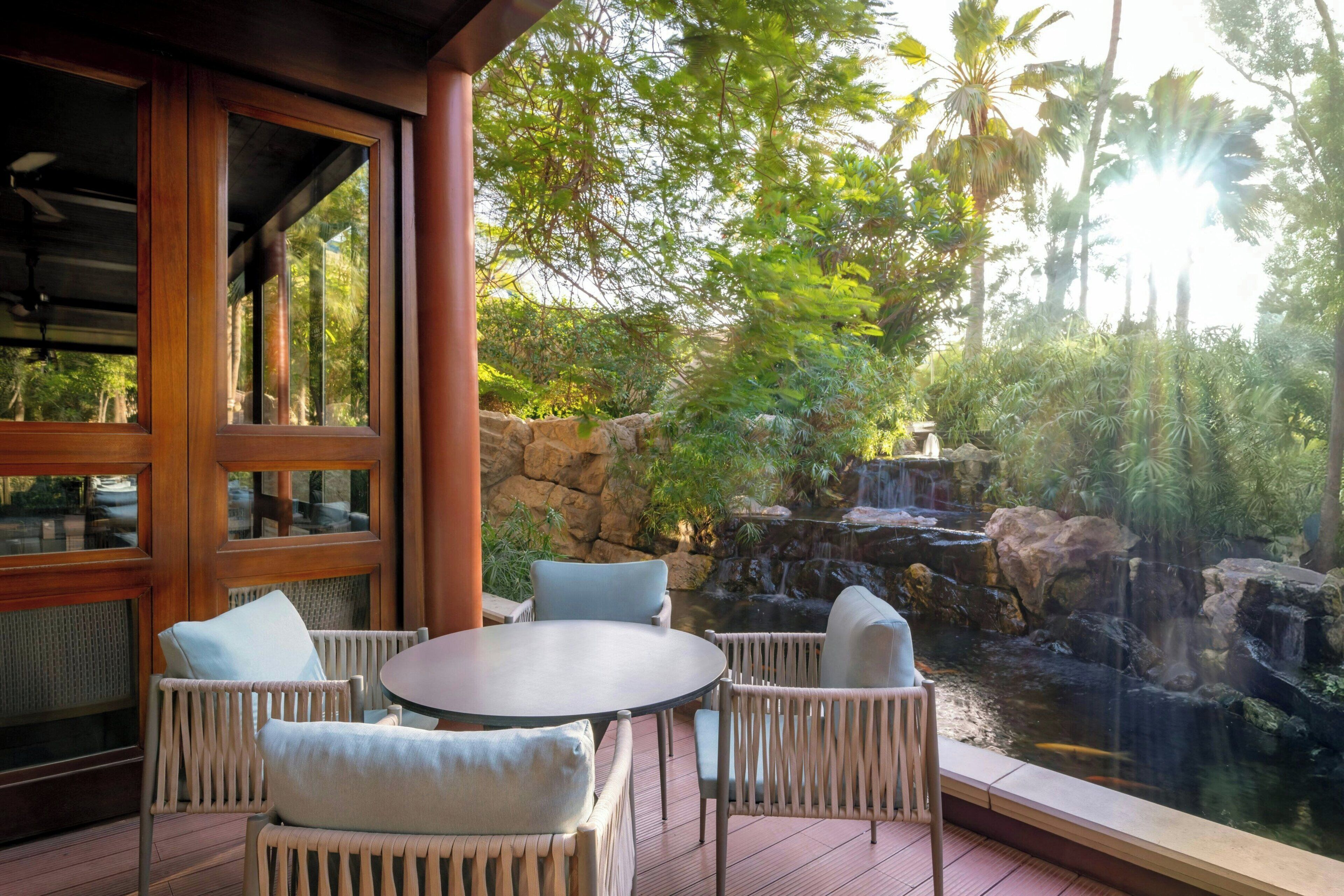 A patio with wicker furniture and a view of a waterfall and pond.
