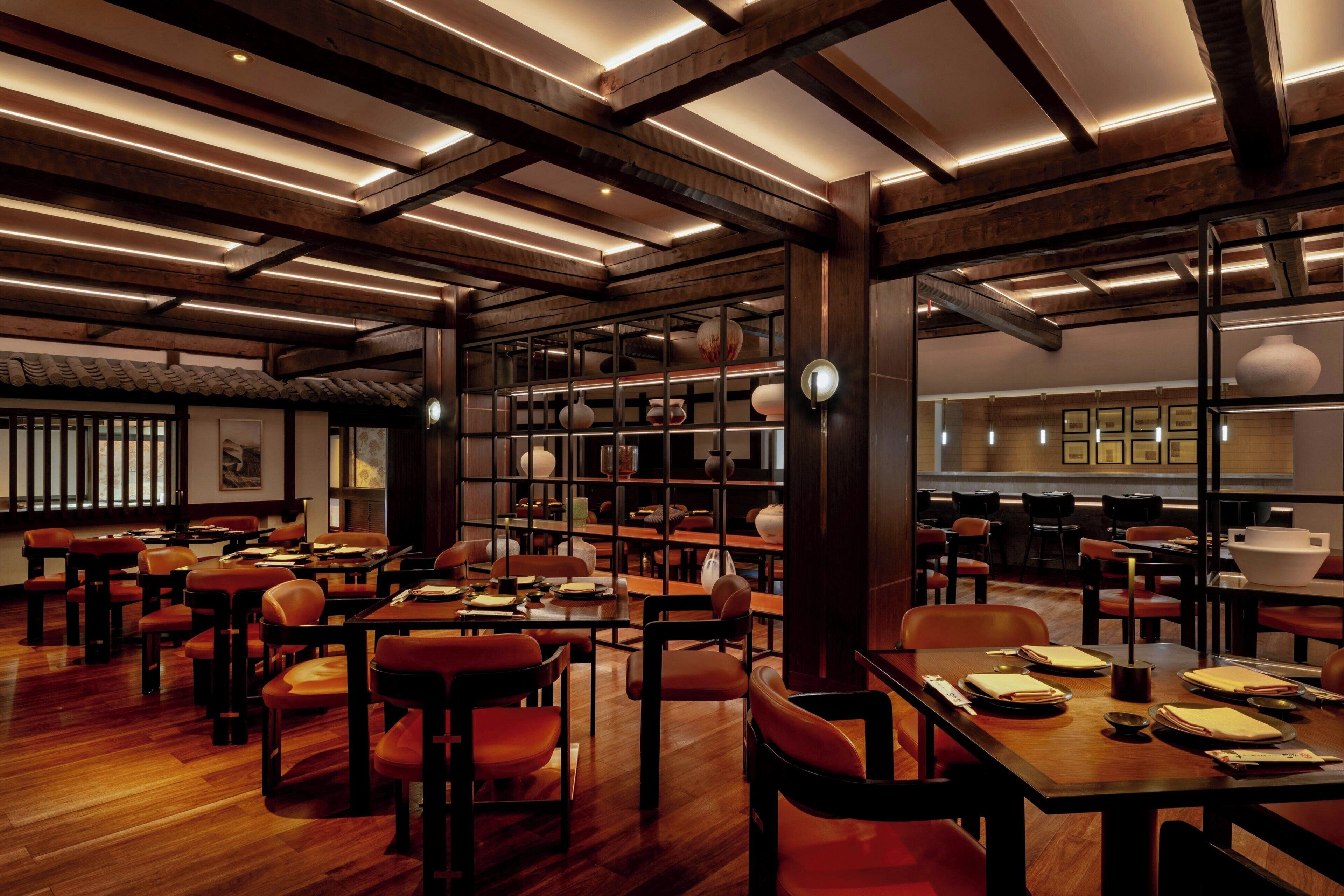 Een ruime restaurantruimte met houten tafels en stoelen, een hoog plafond met zichtbare balken en een traditioneel Aziatisch decor.