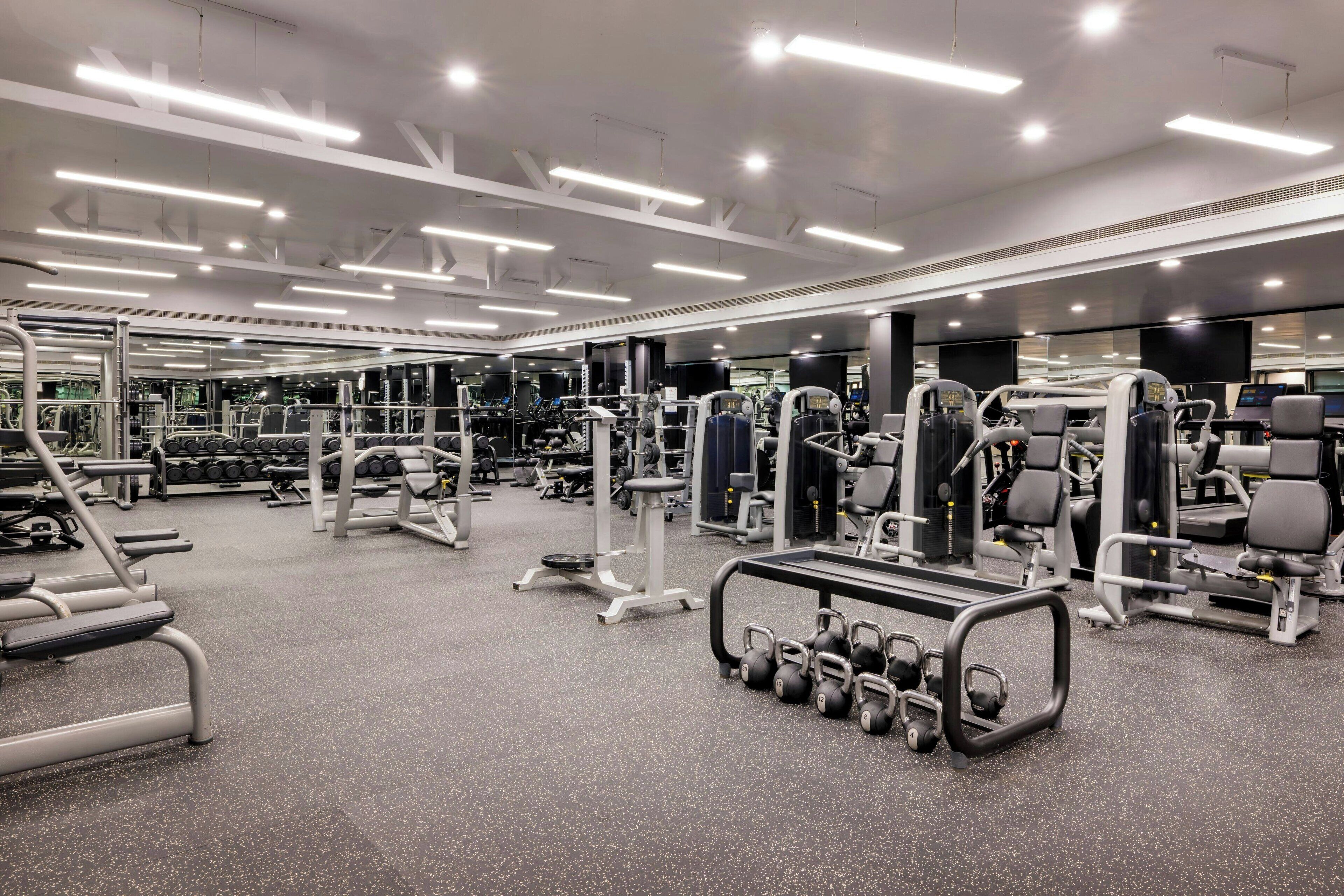 A modern gym with various exercise equipment, mirrored walls, and bright overhead lighting.