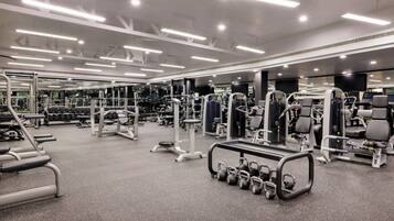 A modern gym with various exercise equipment, mirrored walls, and bright overhead lighting.