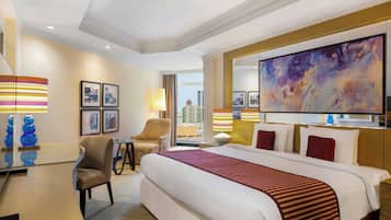 A hotel room with a large bed, a desk, a chair, and a large window offering a city view.