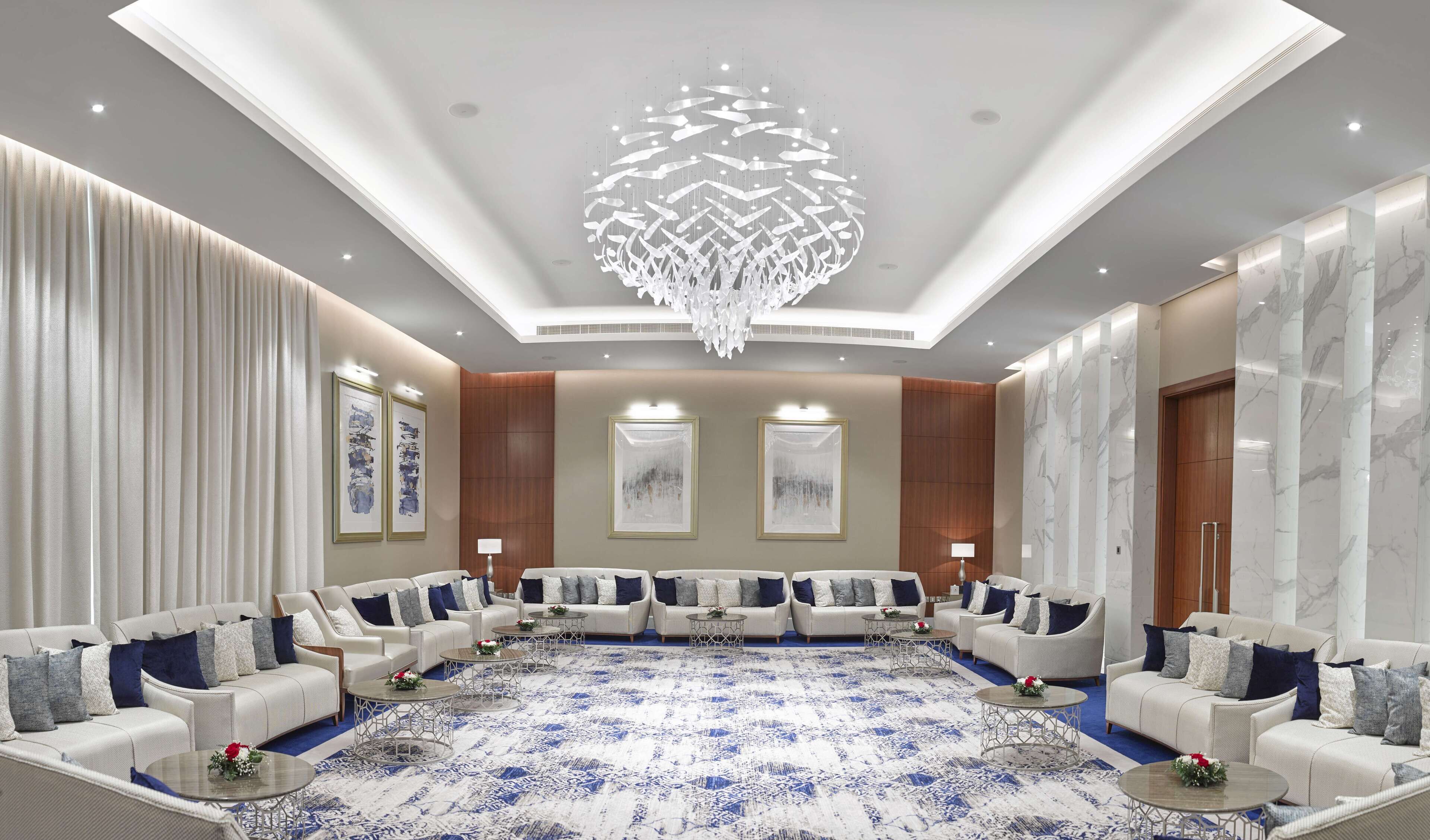 Un'ampia sala conferenze con soffitto alto, un lampadario moderno e una moquette decorata.