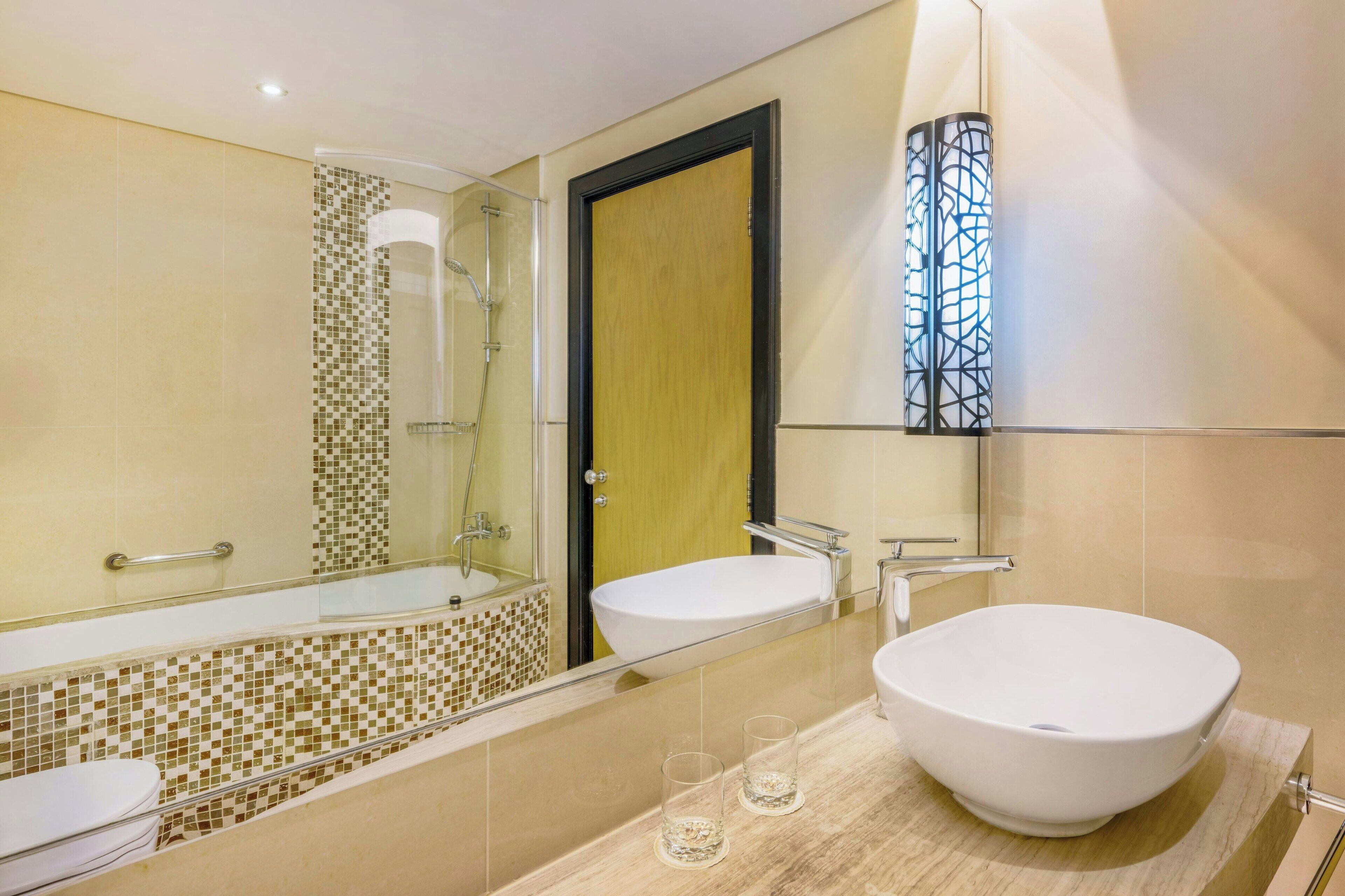 A bathroom with a large mirror, two sinks, a shower, and a mosaic tile backsplash.
