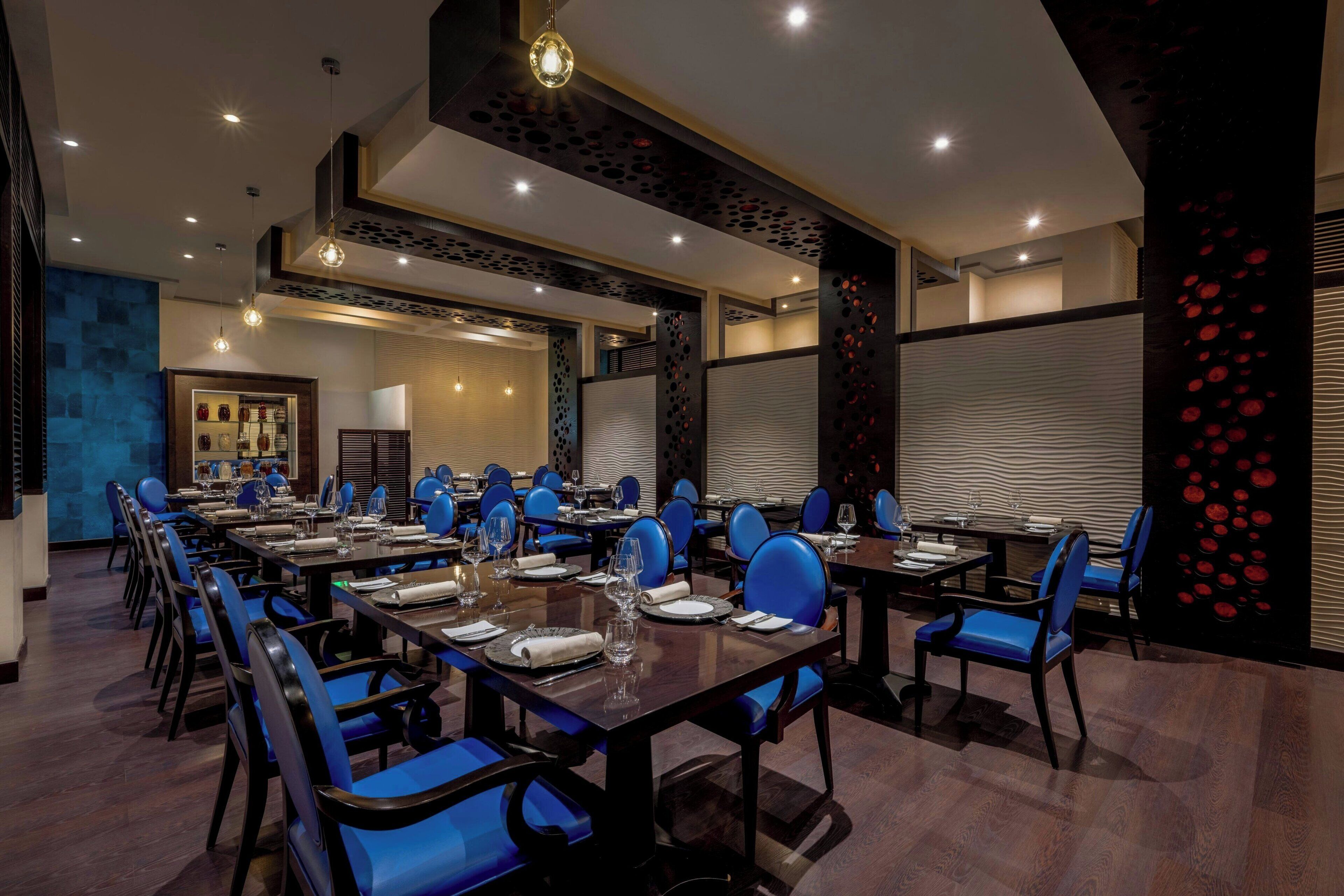 Een moderne eetruimte met blauwe stoelen en tafels, inbouwverlichting en decoratieve wandpanelen.