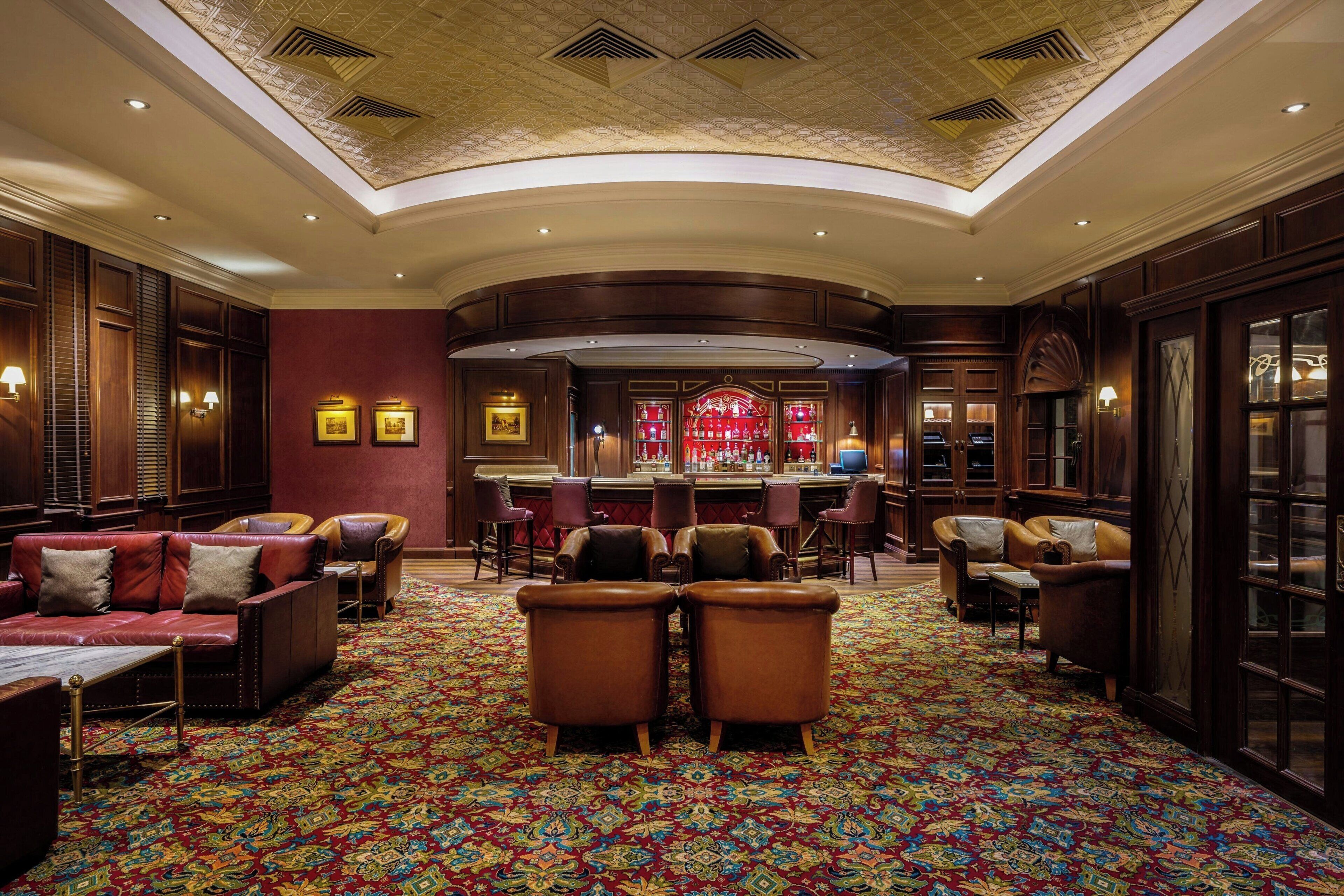A spacious lobby with a patterned carpet, leather seating, a bar area, and a decorative ceiling.