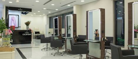 A modern hair salon with multiple stations, a reception desk, and a color bar area.