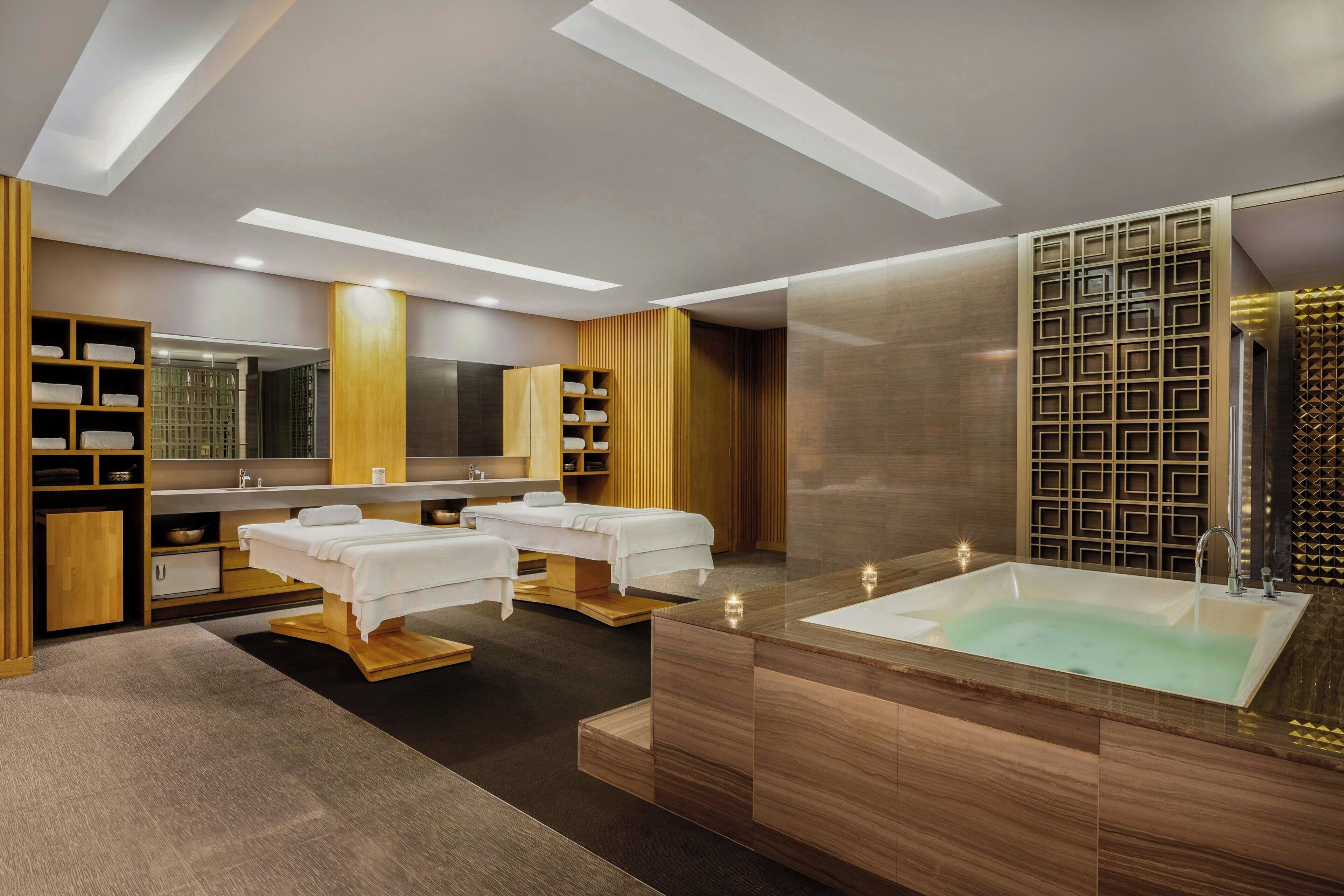 Un spa moderno con una bañera grande, dos camillas de masaje y un tocador de madera con estantes.
