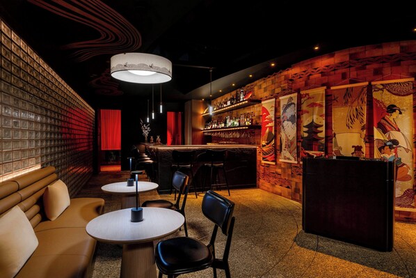 A bar area with a brick wall, a counter with bottles, and a red curtain. There are tables and chairs for seating. - Gulf Hotel Convention and SPA (Manama)