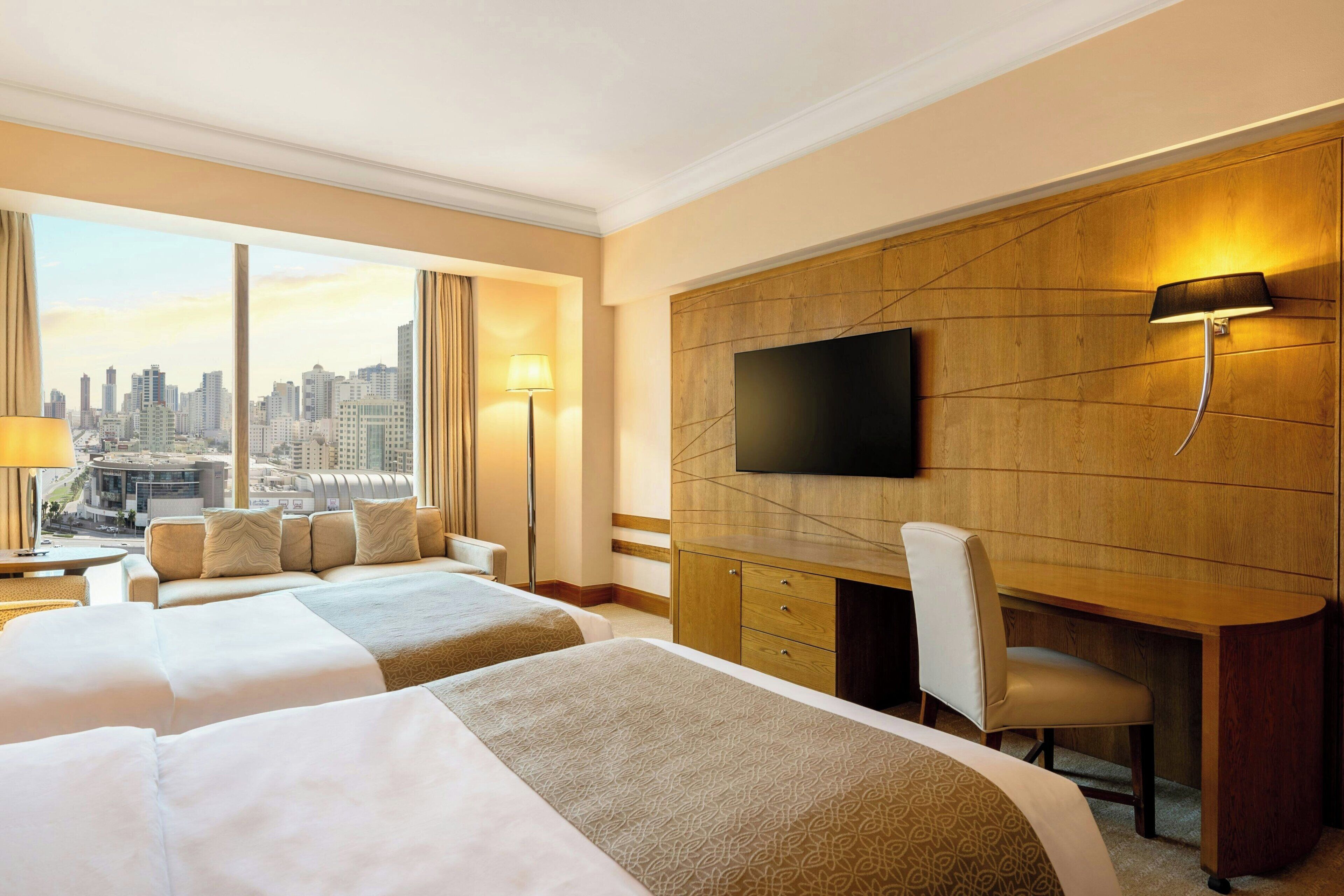 A hotel room with two beds, a desk, a chair, a TV, and a city view.